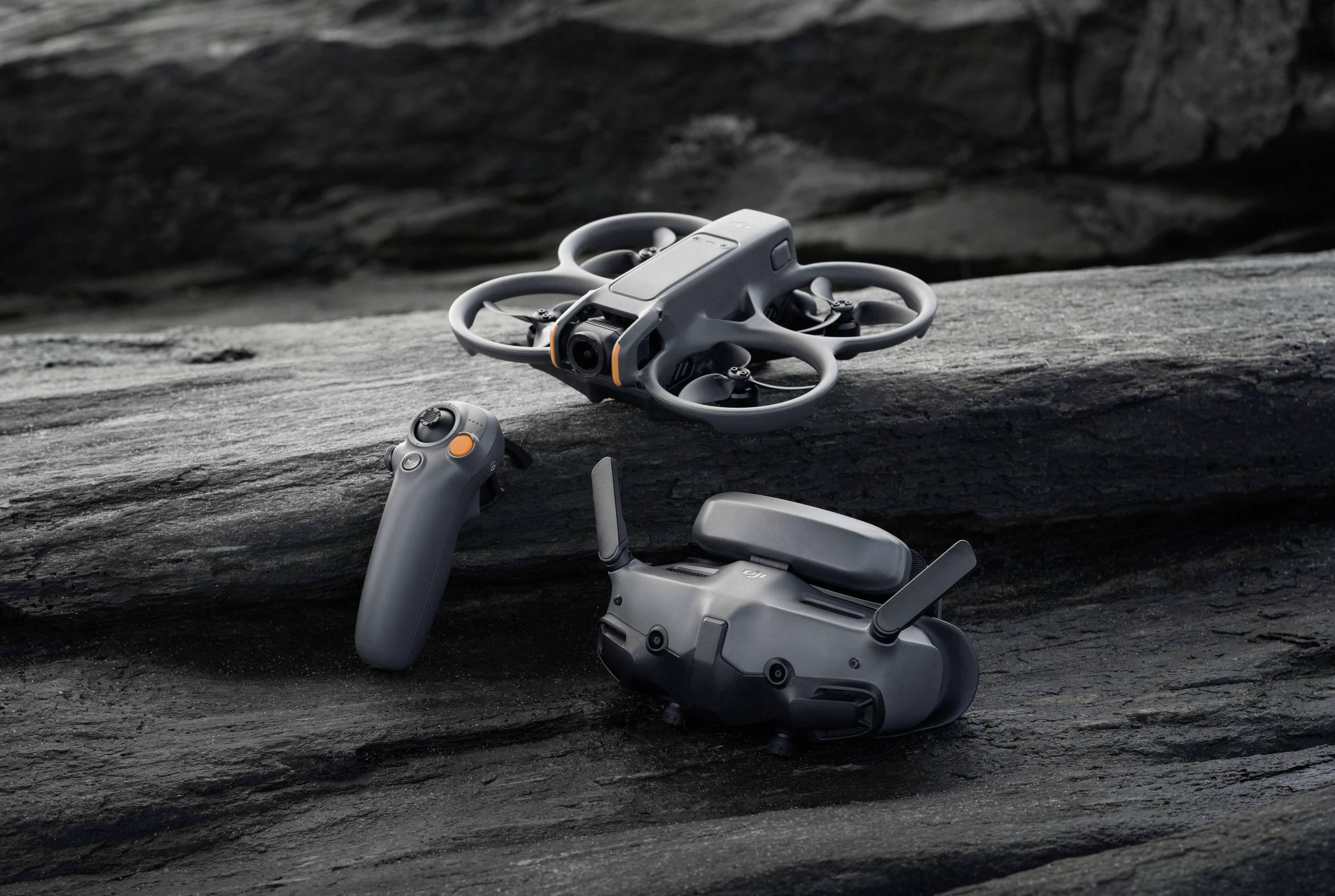 Un drone gris plane au-dessus d'un terrain rocailleux. À côté se trouvent une télécommande et des lunettes de réalité virtuelle.