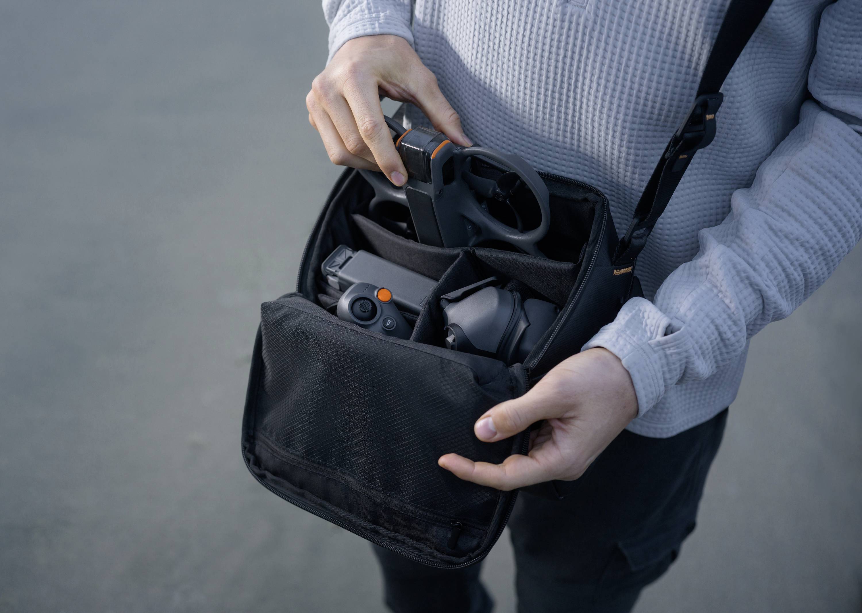 Une personne tient un sac ouvert contenant des accessoires de drone, incluant une caméra et une télécommande.