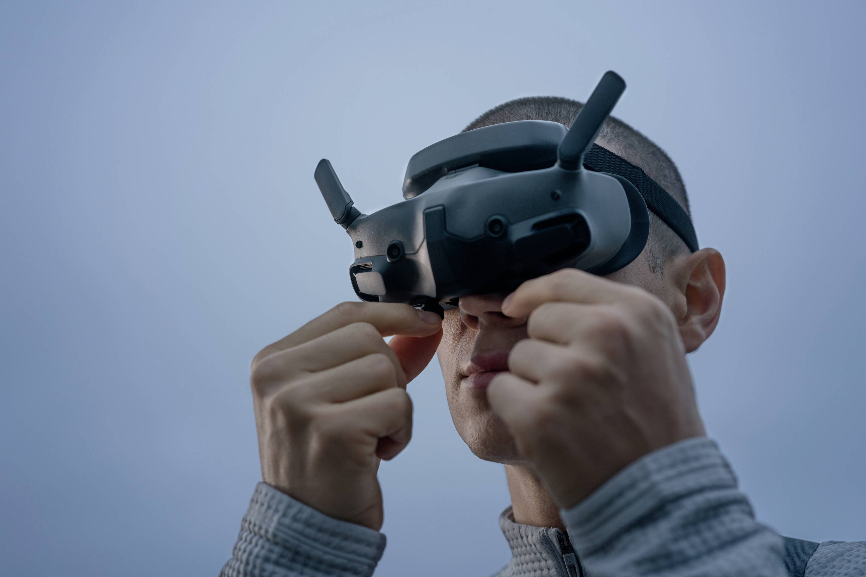 Une personne porte un casque de réalité virtuelle et le tient fermement. L'arrière-plan est bleu et sans nuages.
