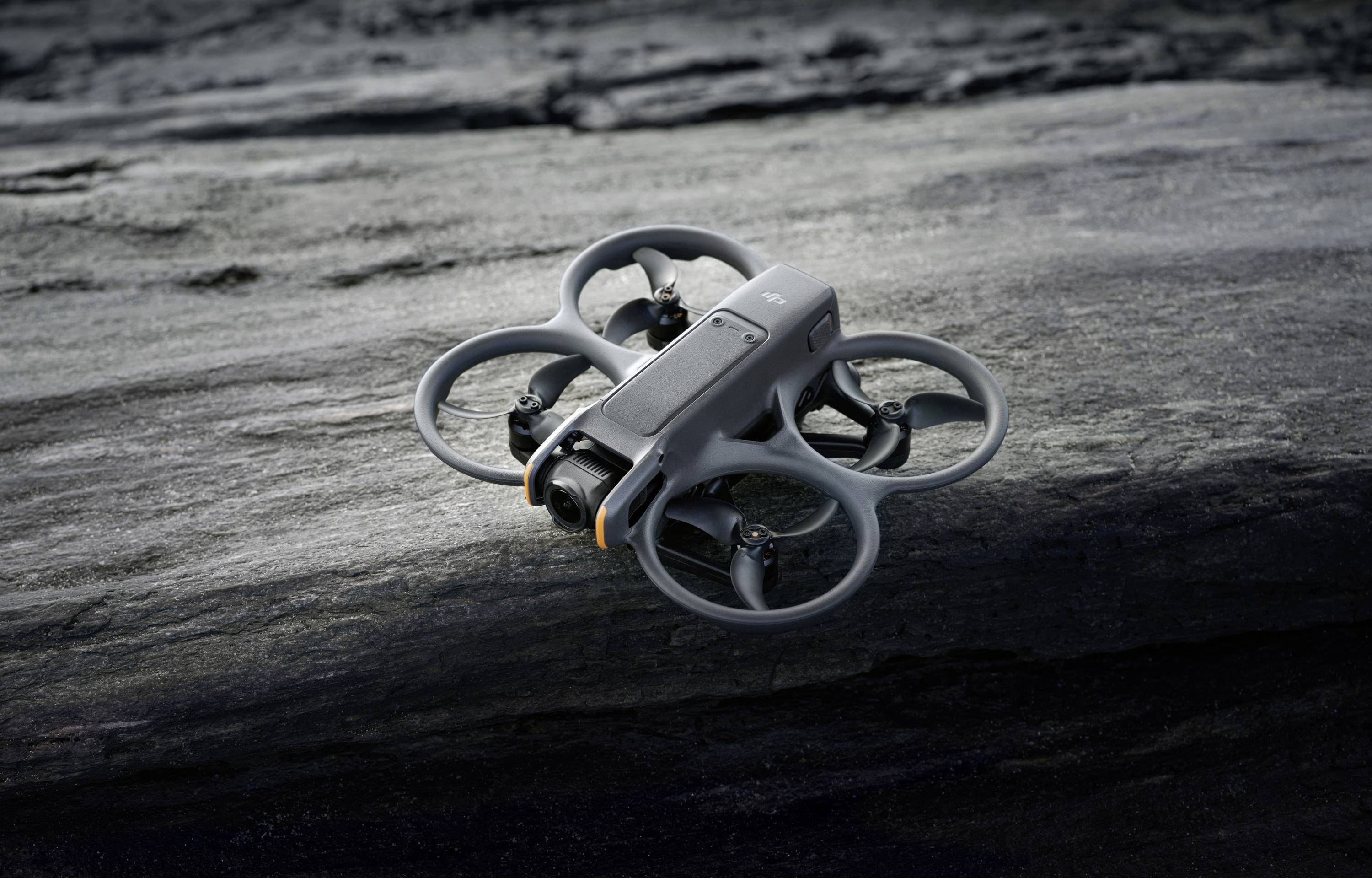 Un drone gris repose sur une surface rocheuse. Il possède quatre rotors munis de protections. La scène suggère une utilisation en extérieur.