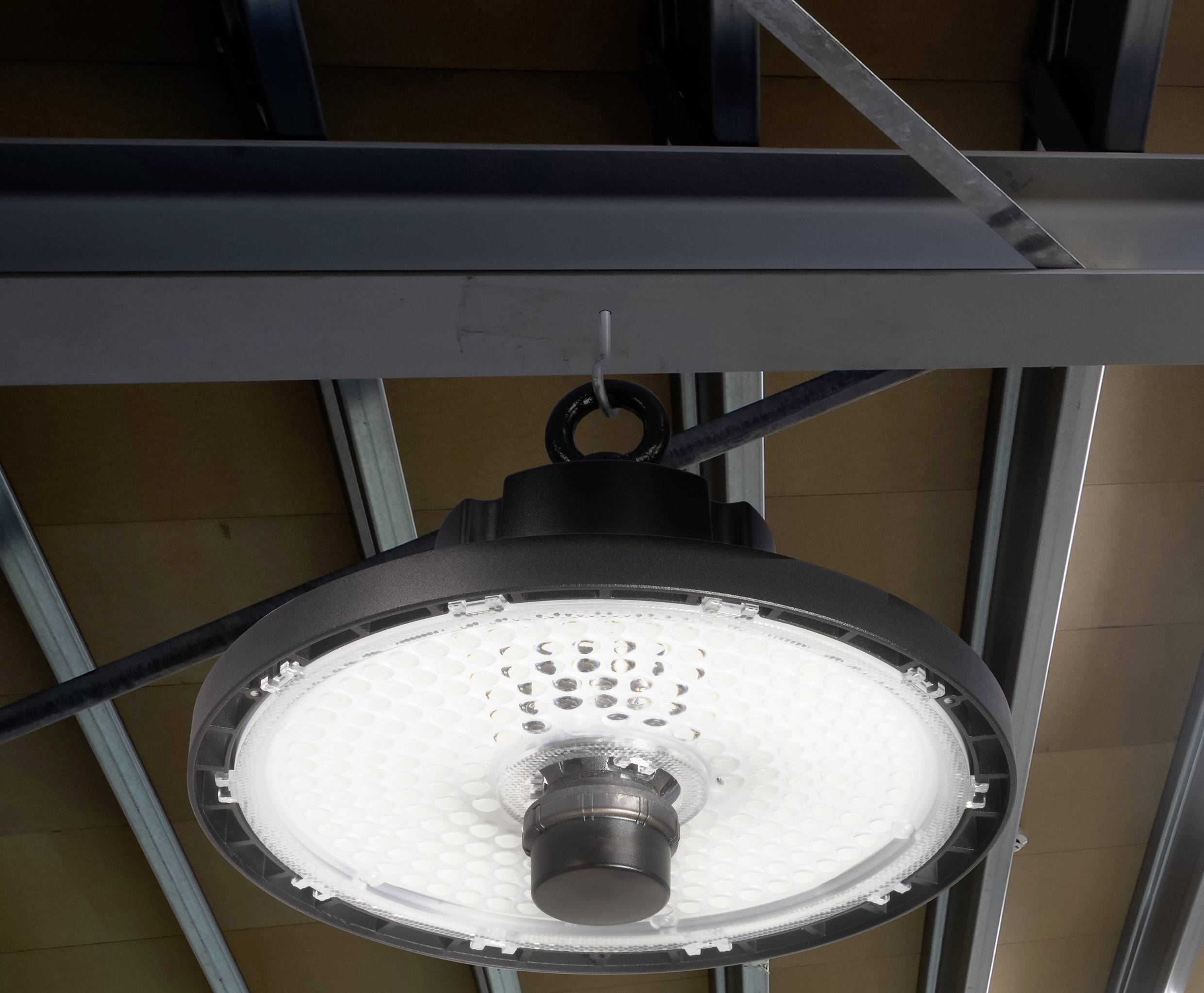 Une lampe LED ronde est suspendue à un plafond en métal. La lampe est allumée et brille dans un environnement industriel.