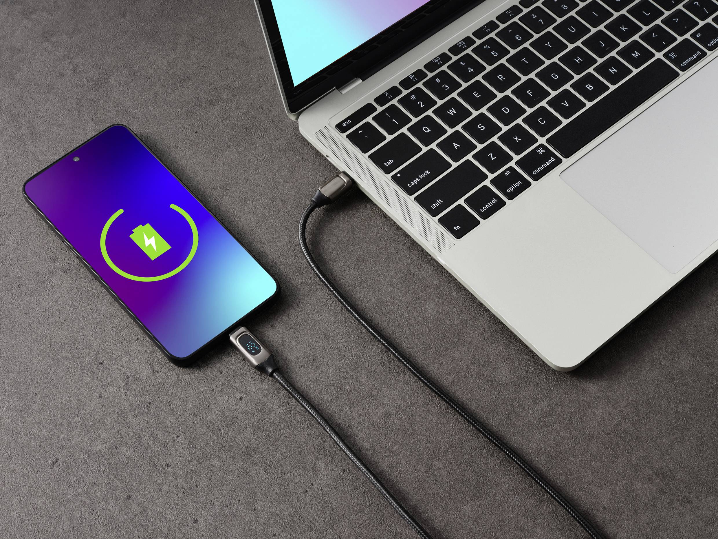 Un smartphone se charge via un câble USB connecté à un ordinateur portable. L'écran du smartphone affiche un symbole de charge.