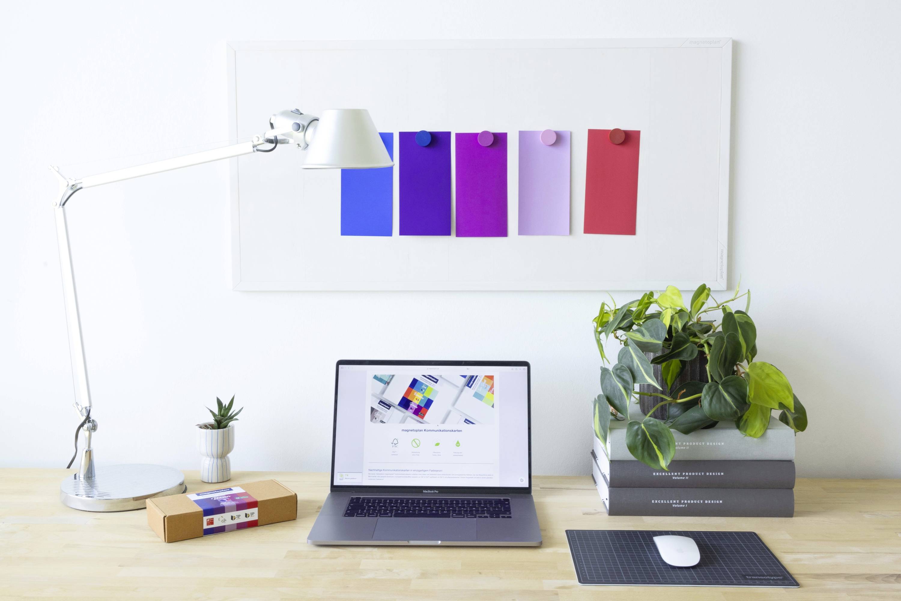 Un bureau bien rangé avec un ordinateur portable, une lampe de bureau, des plantes et des motifs colorés sur le mur en arrière-plan.