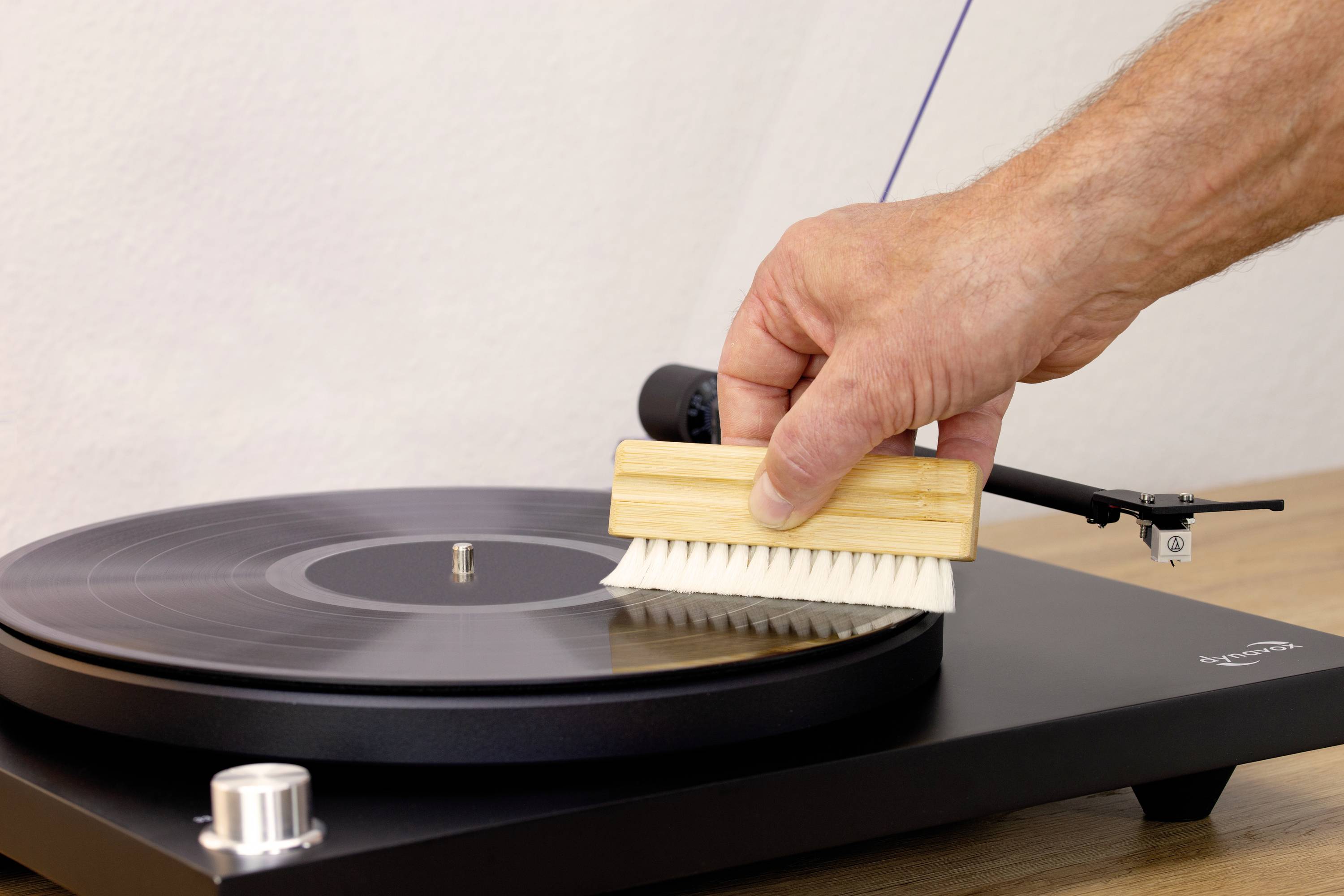 Une main nettoie un disque vinyle avec une brosse sur une platine tourne-disque.