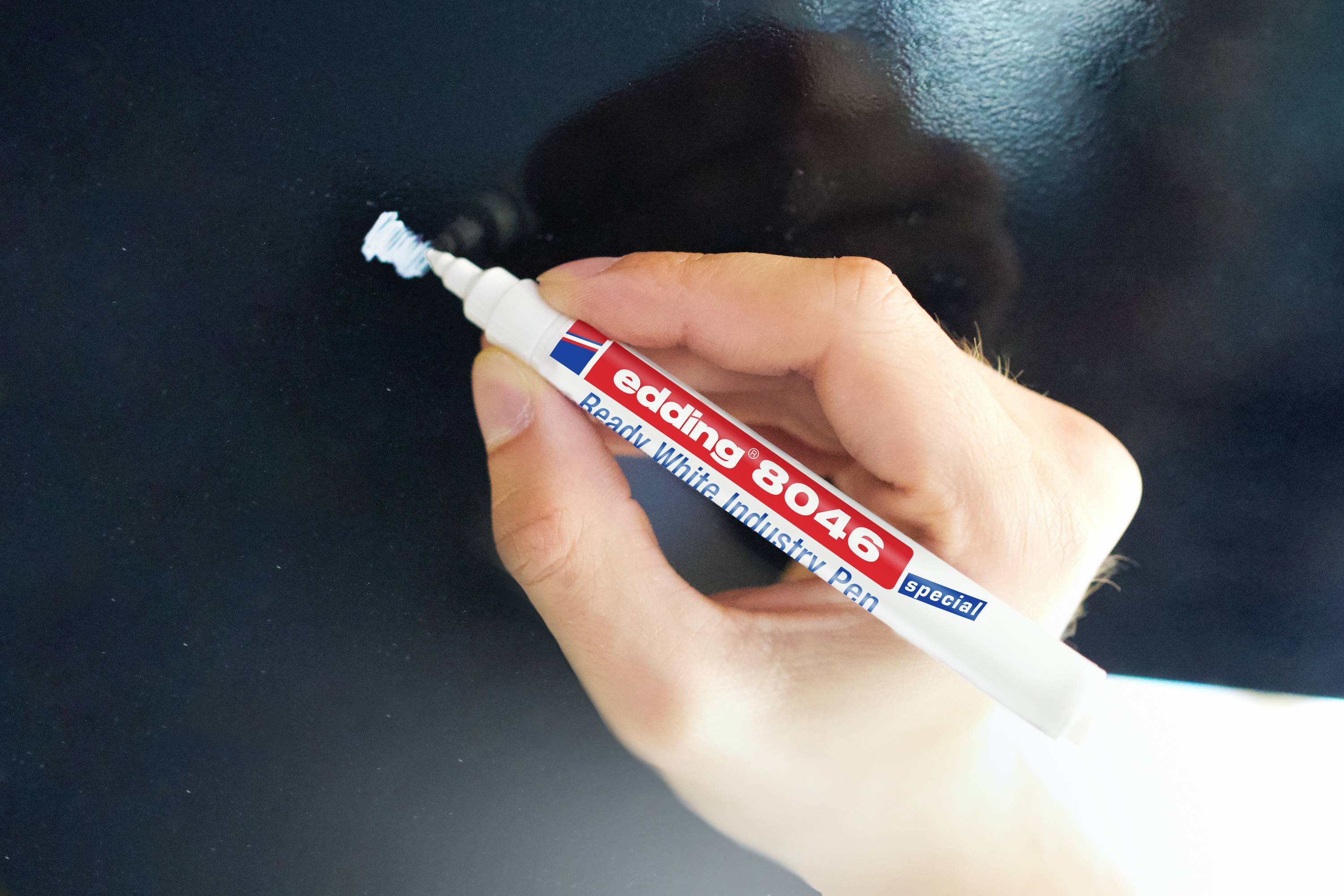 Une main écrit avec un marqueur blanc sur un tableau.