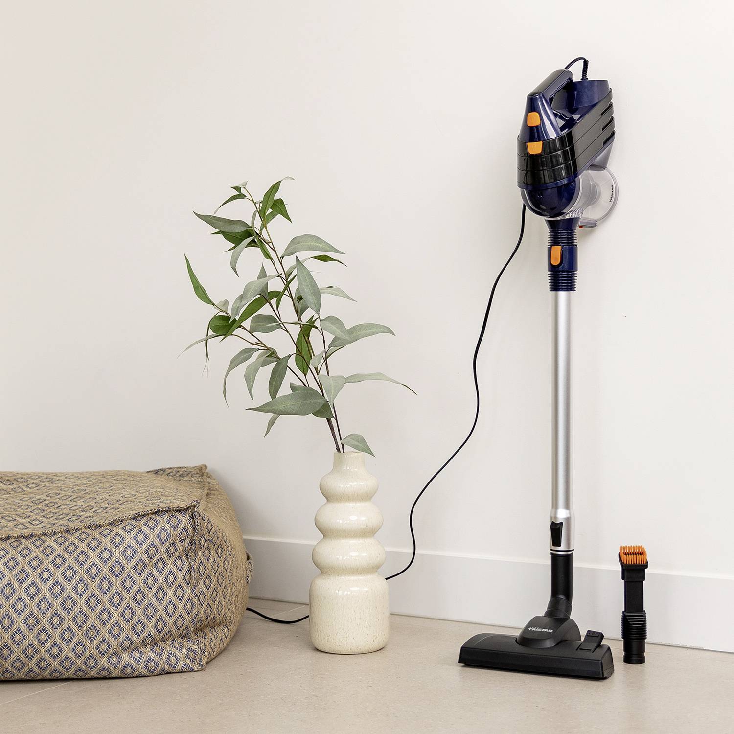 Aspirateur traîneau dans une pièce, posé à côté d'un coussin et d'une plante d'intérieur sur une table.