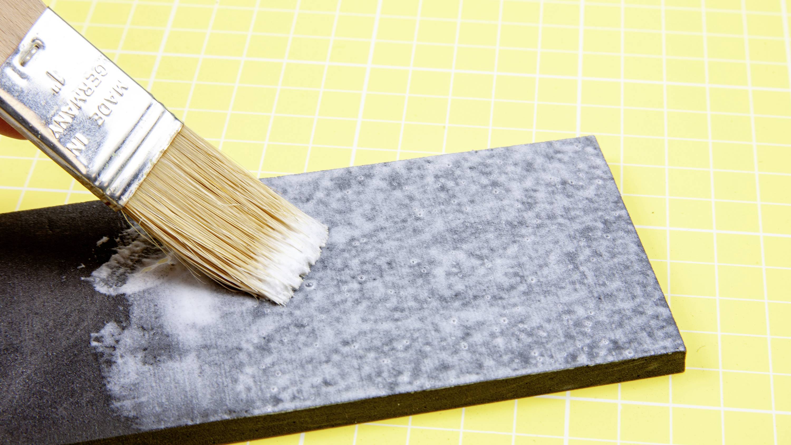 Un pinceau applique de la peinture blanche sur un rectangle noir sur un fond jaune avec une grille.