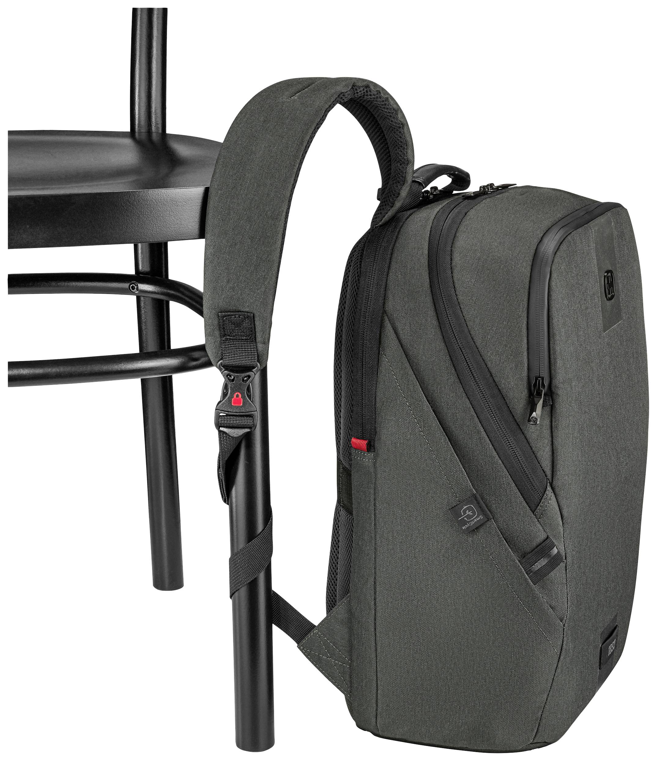 Un sac à dos gris est accroché à une chaise noire, fixé par une sangle. Le sac à dos possède plusieurs compartiments et une fermeture éclair.