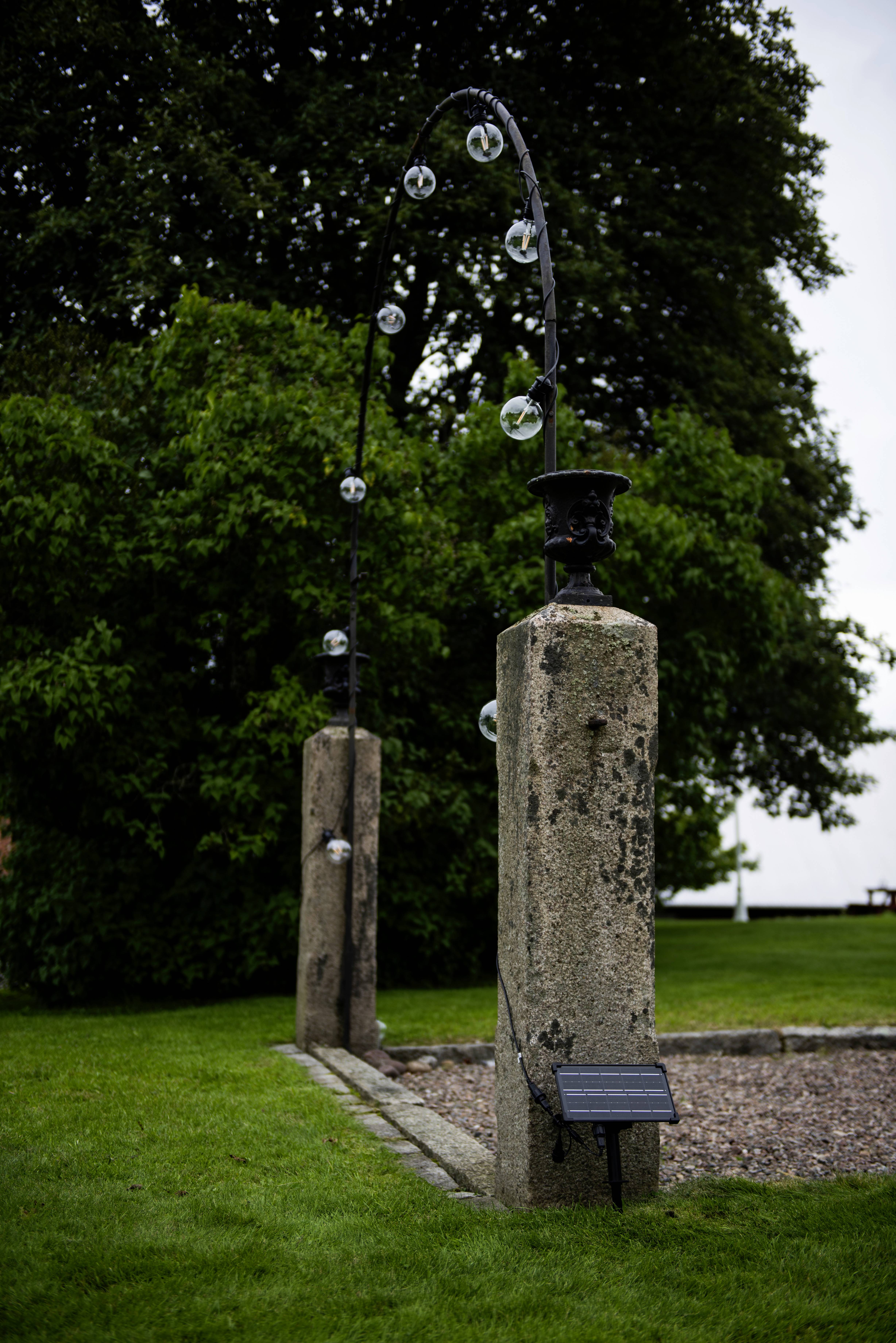 Une construction arquée en pierre avec plusieurs boules de verre posées dessus, placée à l'extérieur sur une pelouse verte à côté de grands arbres.
