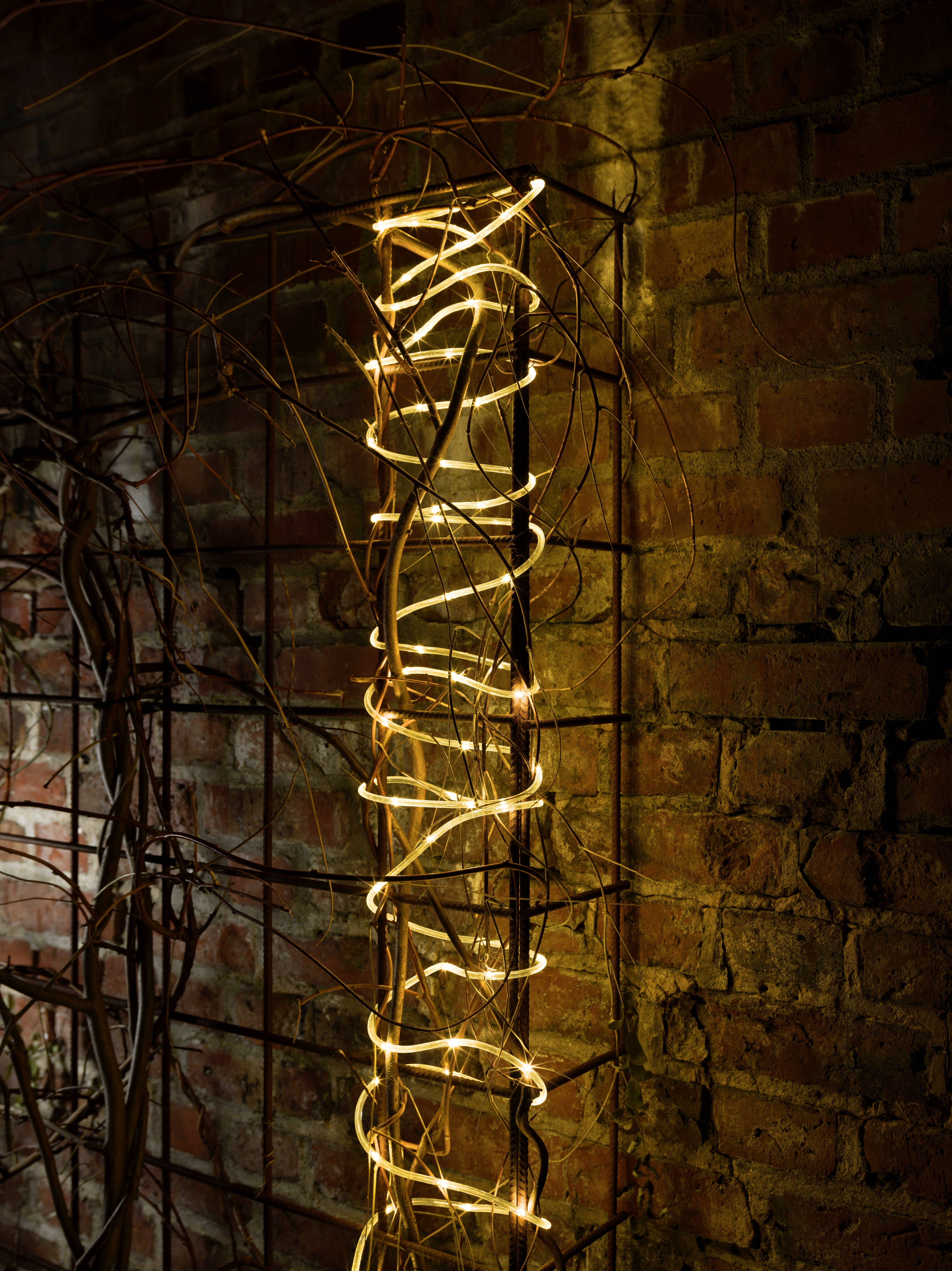 Les guirlandes lumineuses sont enroulées autour d'un treillis contre un mur de briques, créant une lumière chaleureuse et accueillante.