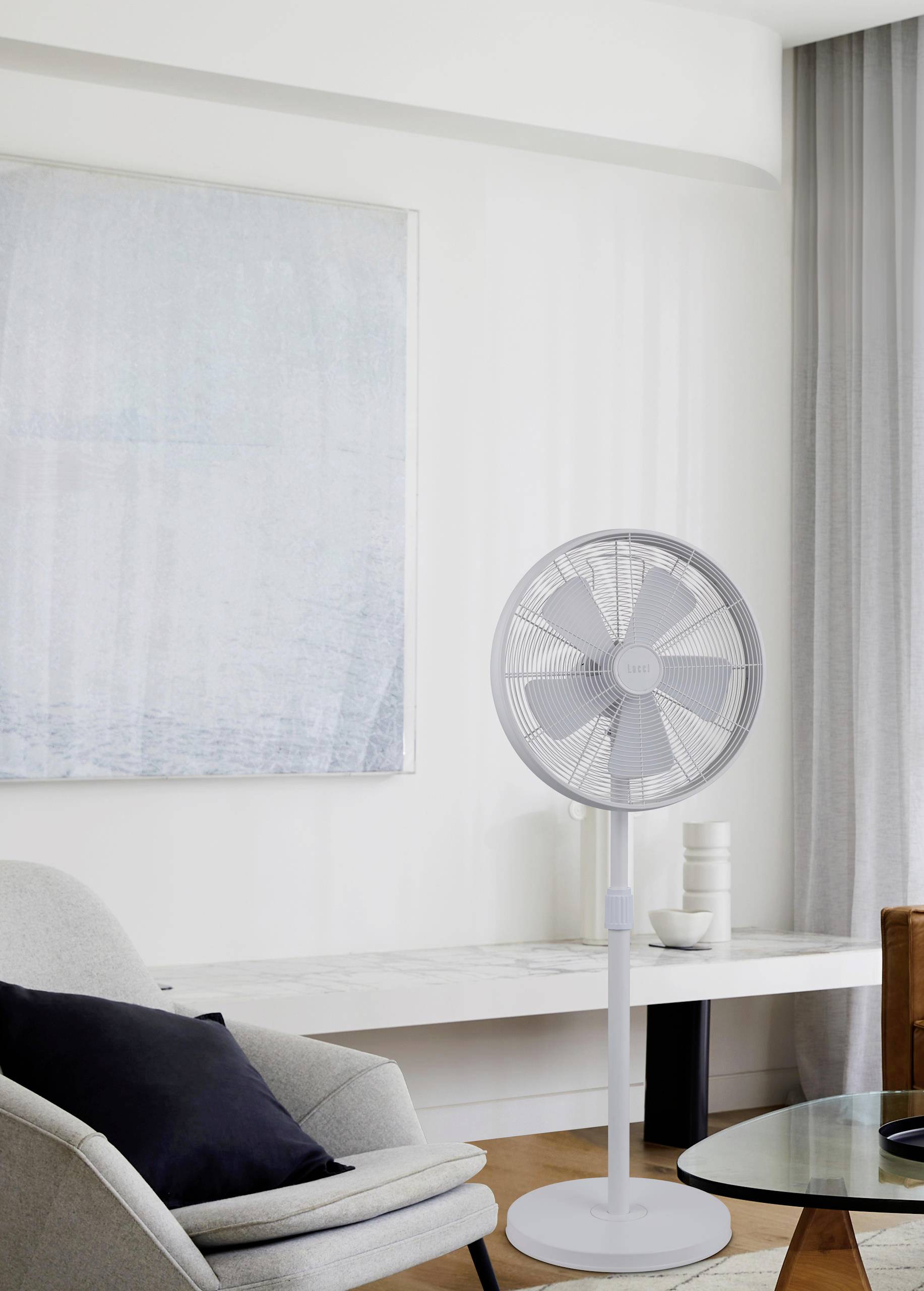 Un salon avec un ventilateur sur pied blanc à côté d'un fauteuil, d'une table et d'un grand tableau accroché au mur.