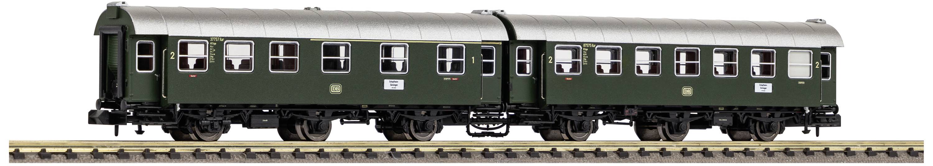 Train miniature vert avec deux wagons sur des rails, vue latérale.