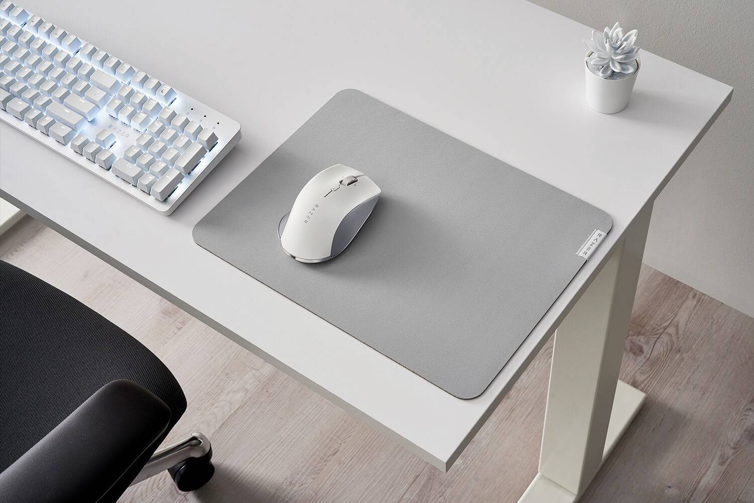 Un bureau minimaliste avec un clavier blanc, une souris grise sur un tapis de souris gris et une petite plante dans un pot blanc.