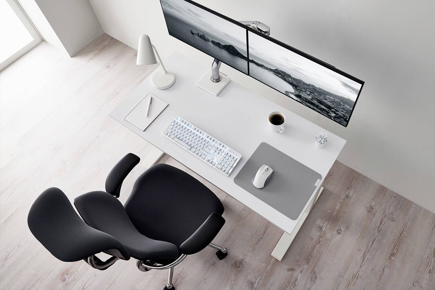 Un bureau moderne et bien rangé avec deux écrans, un clavier, une souris, un bloc-notes et une tasse de café. Une chaise ergonomique est placée devant.