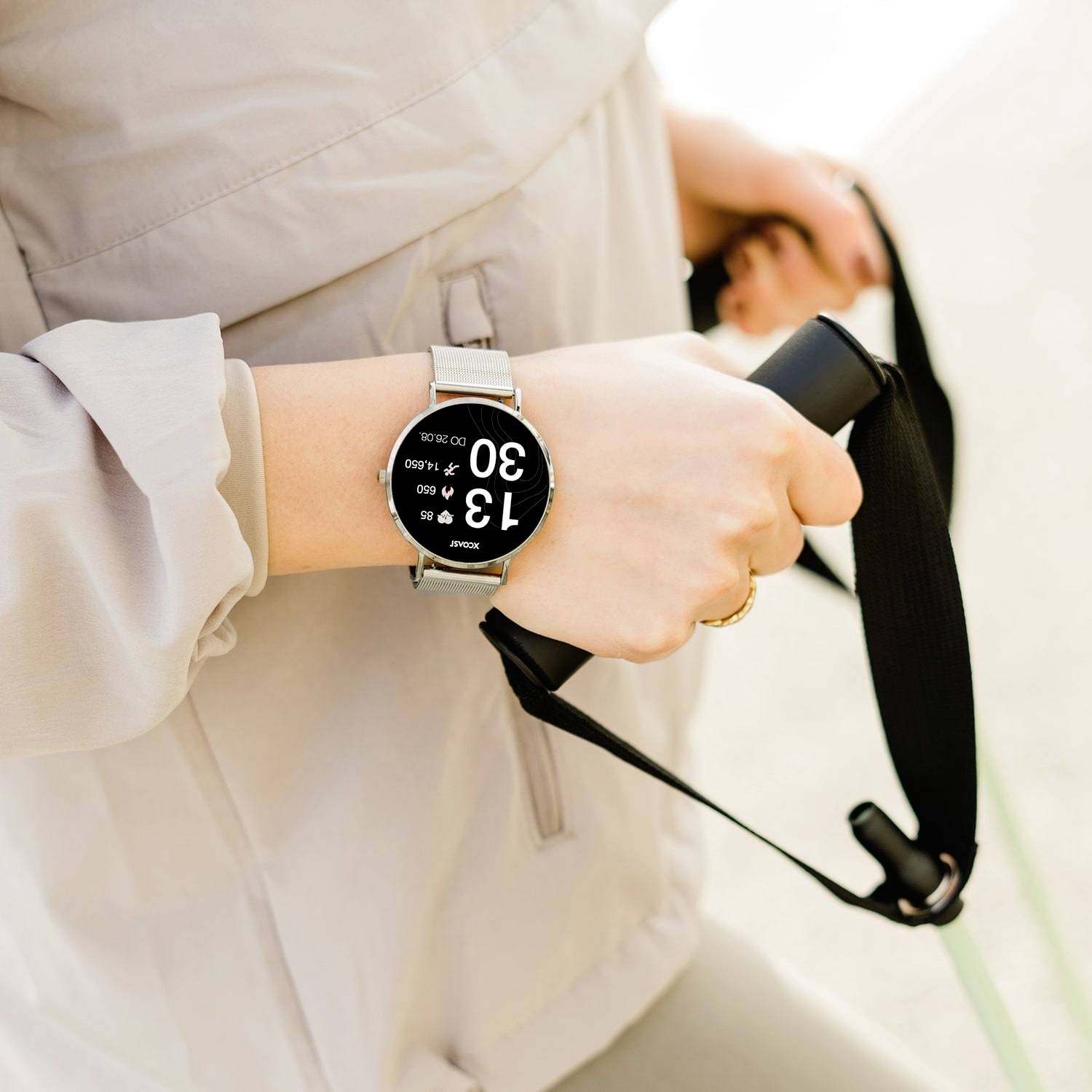 Une personne portant un tracker de fitness, affichant ses pas et sa fréquence cardiaque. La personne tient un bracelet d'activité. Activité en extérieur.