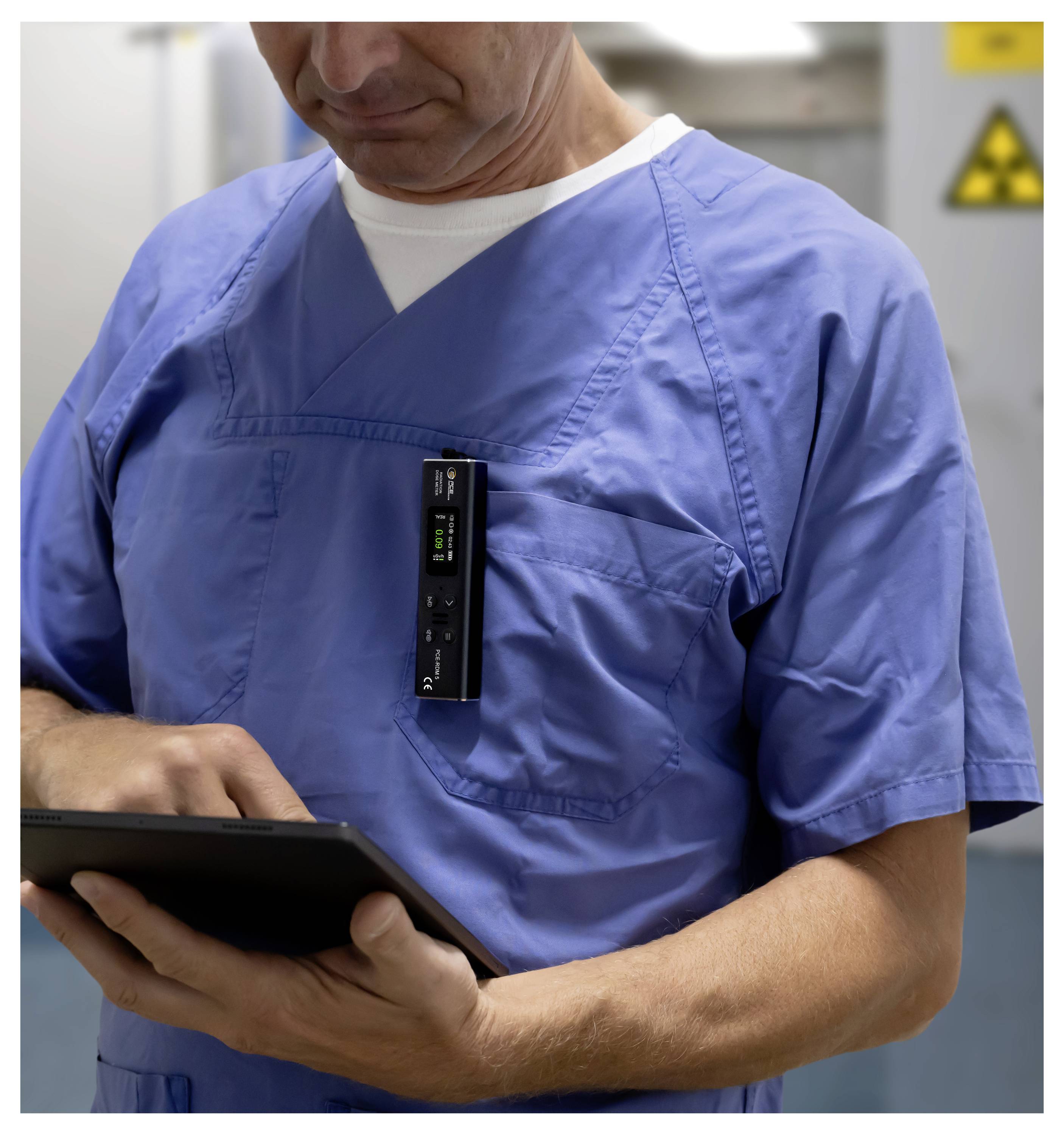 Un professionnel de la santé en blouse bleue utilise une tablette, avec un dispositif électronique attaché sur sa poitrine dans un environnement hospitalier.