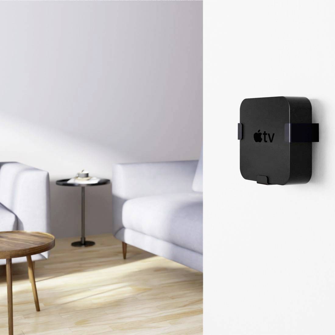 Une boîte TV noire arborant le logo Apple est montée sur le mur blanc d'un salon moderne. À l'arrière-plan, on aperçoit une table et un canapé.