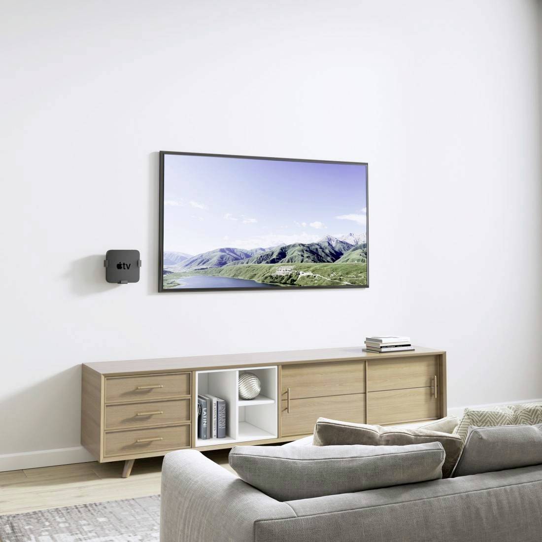 Un salon avec un canapé, un meuble TV en bois et un téléviseur à écran plat accroché au mur, montrant un paysage.