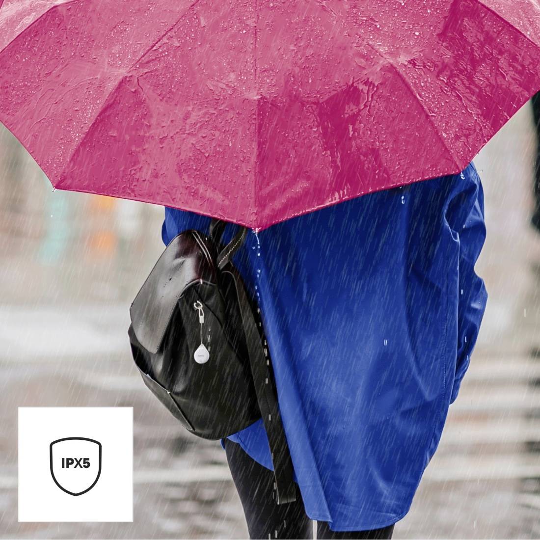 Une personne portant un parapluie rose, vêtue d'une veste bleue et tenant un sac noir, marche sous la pluie. Un symbole IPX5 est situé en bas à gauche.