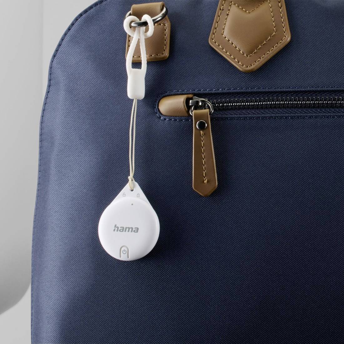 Un tracker rond et blanc est accroché à un sac en tissu bleu avec des détails en cuir marron.