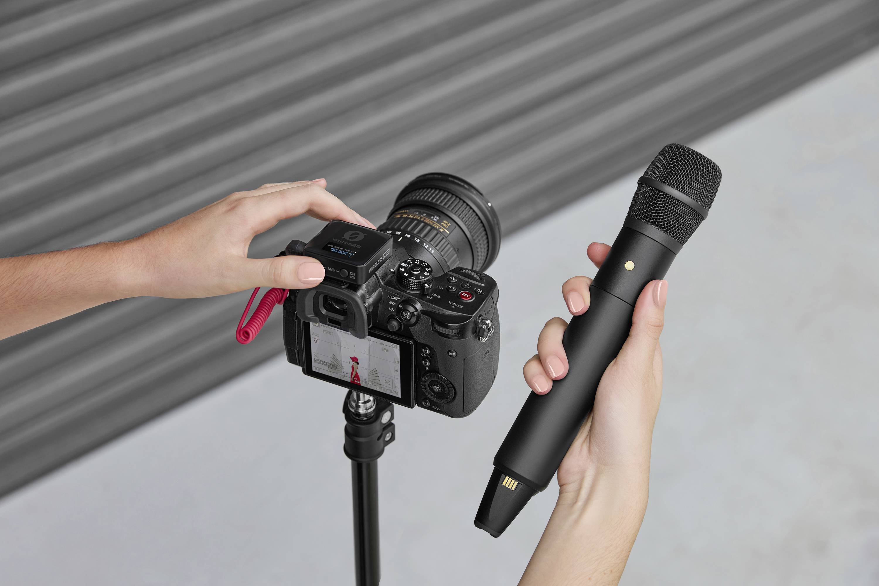 Une personne tient un microphone et manipule une caméra installée sur un trépied, préparée pour des prises de vue vidéo ou photographiques.