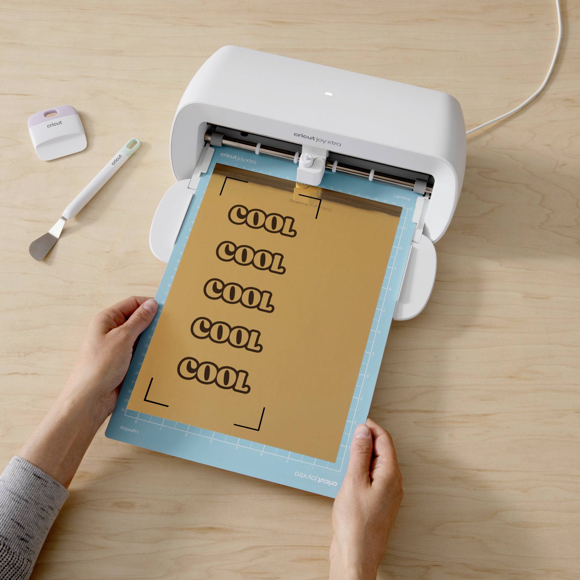 Une personne utilise un traceur de découpe pour découper le mot 'COOL' plusieurs fois sur une feuille de papier.