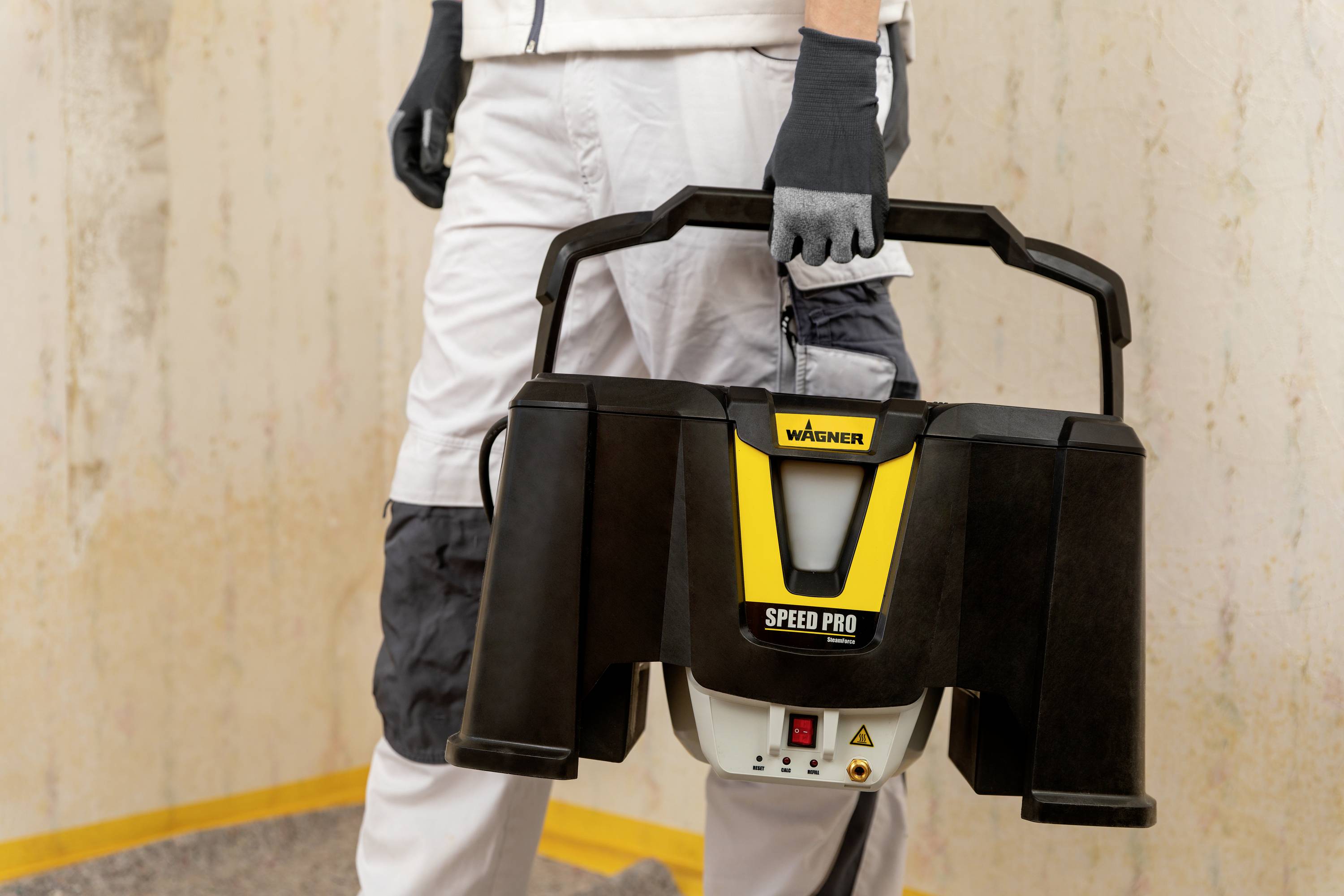 Une personne tient un appareil noir portant l'inscription 'Wagner Speed Pro'. L'appareil semble fonctionnel, probablement destiné à des travaux artisanaux.