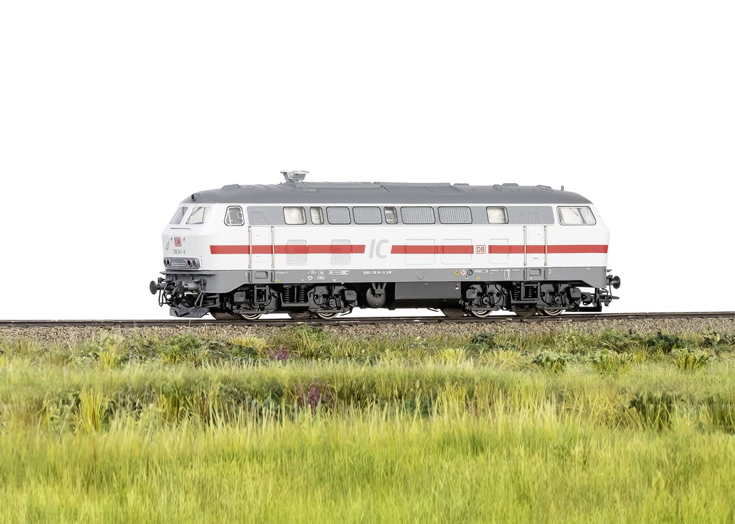 Un modèle d'un train Intercity gris argenté sur une section de voie ferrée, entouré d'herbe verte.