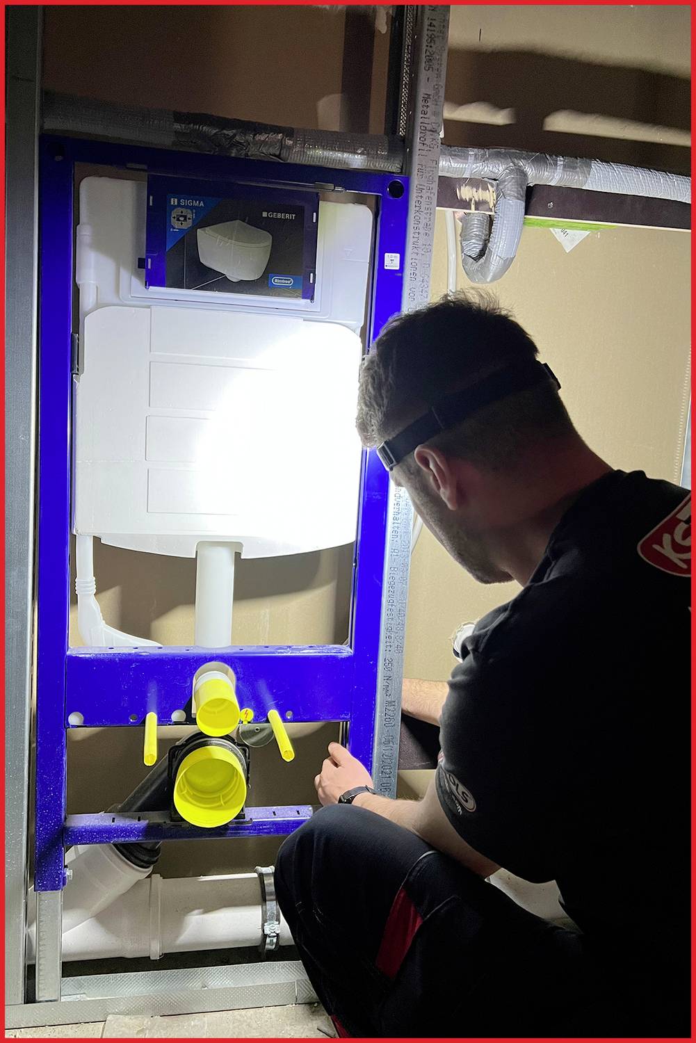 Un homme travaille sur des toilettes encastrées dans un bâtiment en construction. Il porte une lampe frontale et des outils sont visibles.