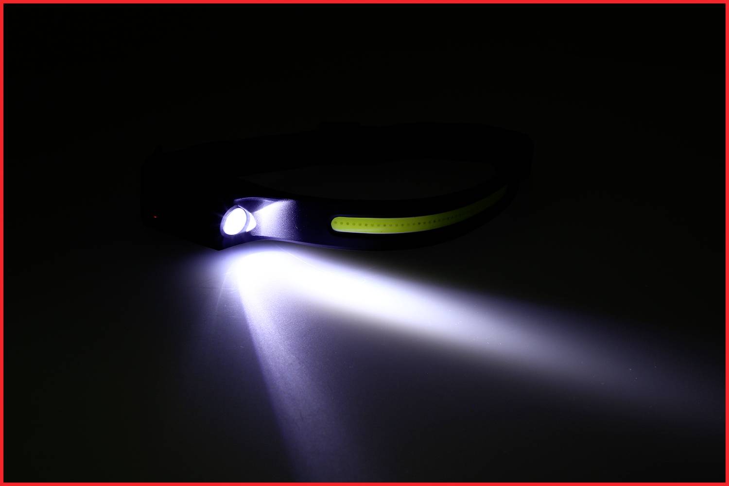 Une lampe frontale allumée repose sur un fond sombre, projetant un faisceau lumineux puissant vers l'avant, la lumière étant blanche et vive.