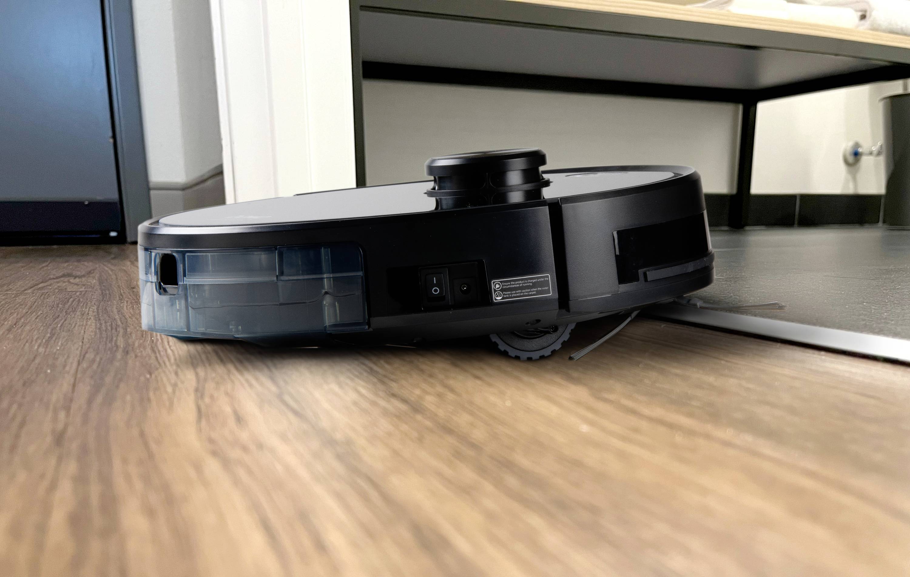 Un robot aspirateur circule sur un plancher en bois et franchit un petit seuil.