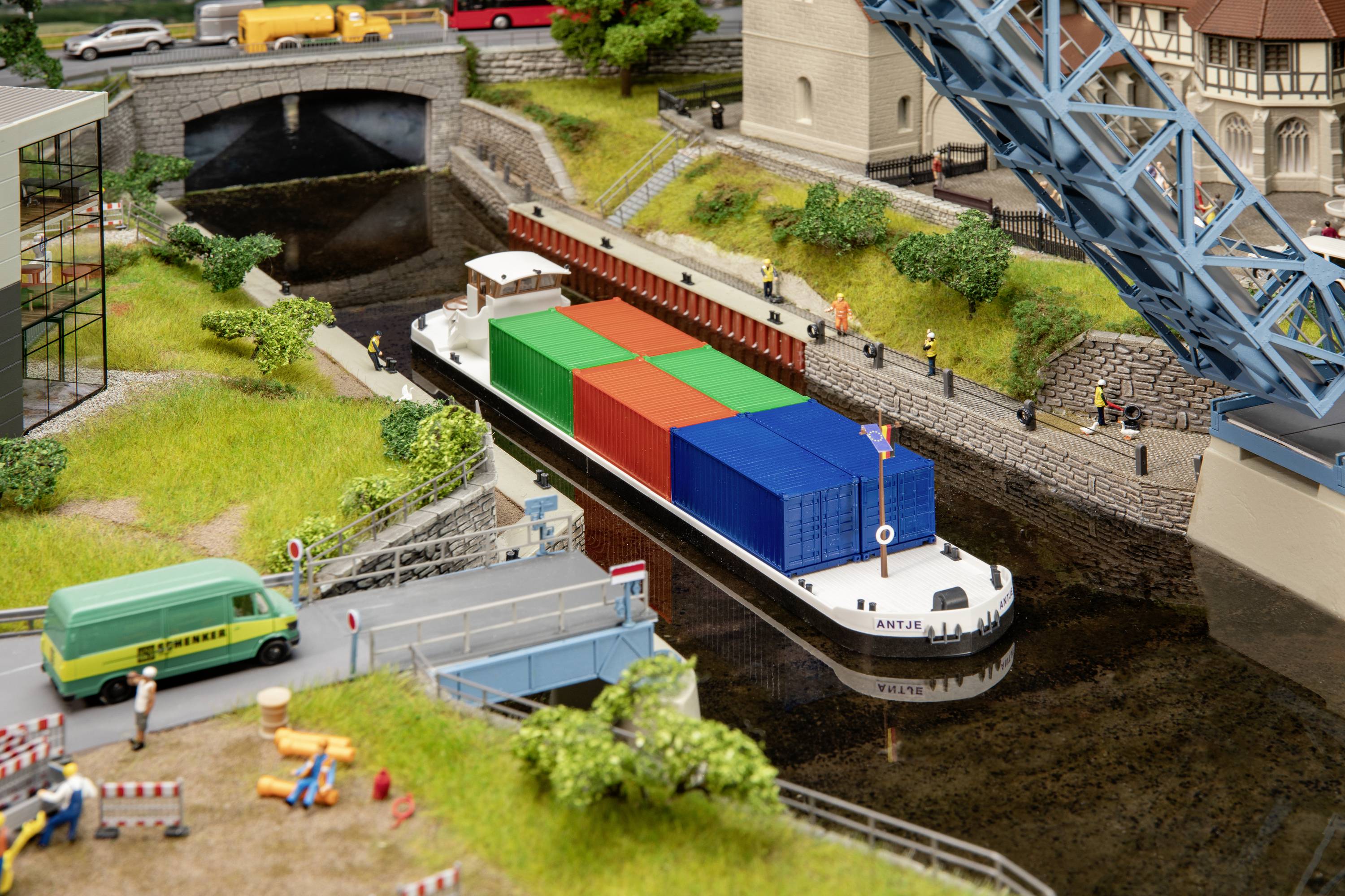 Un cargo transporte des conteneurs colorés à travers un canal avec un pont mobile. Des bâtiments et des véhicules entourent le canal.