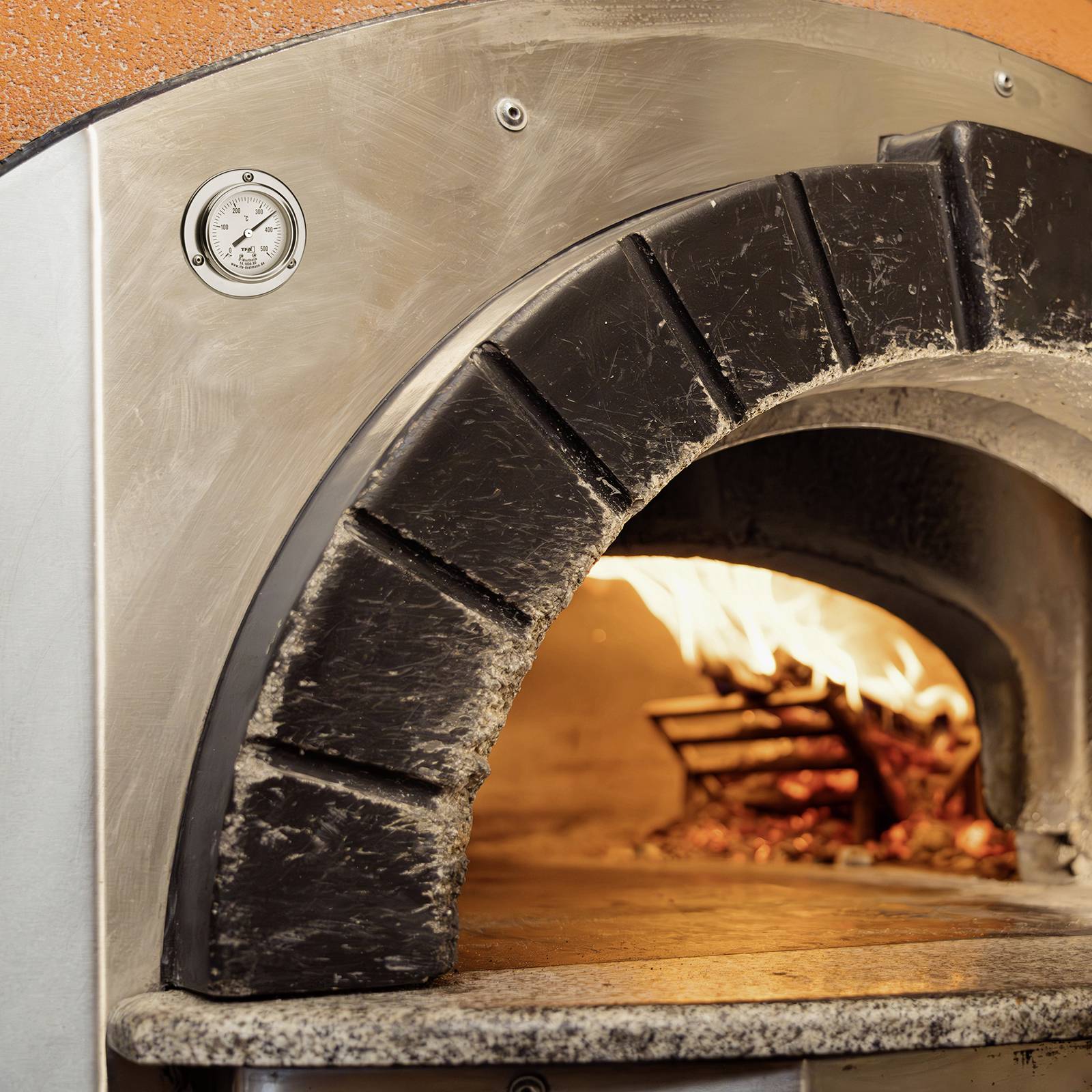 Un four traditionnel en bois avec du bois brûlant et des flammes, adapté pour la cuisson de pizzas ou de pain.