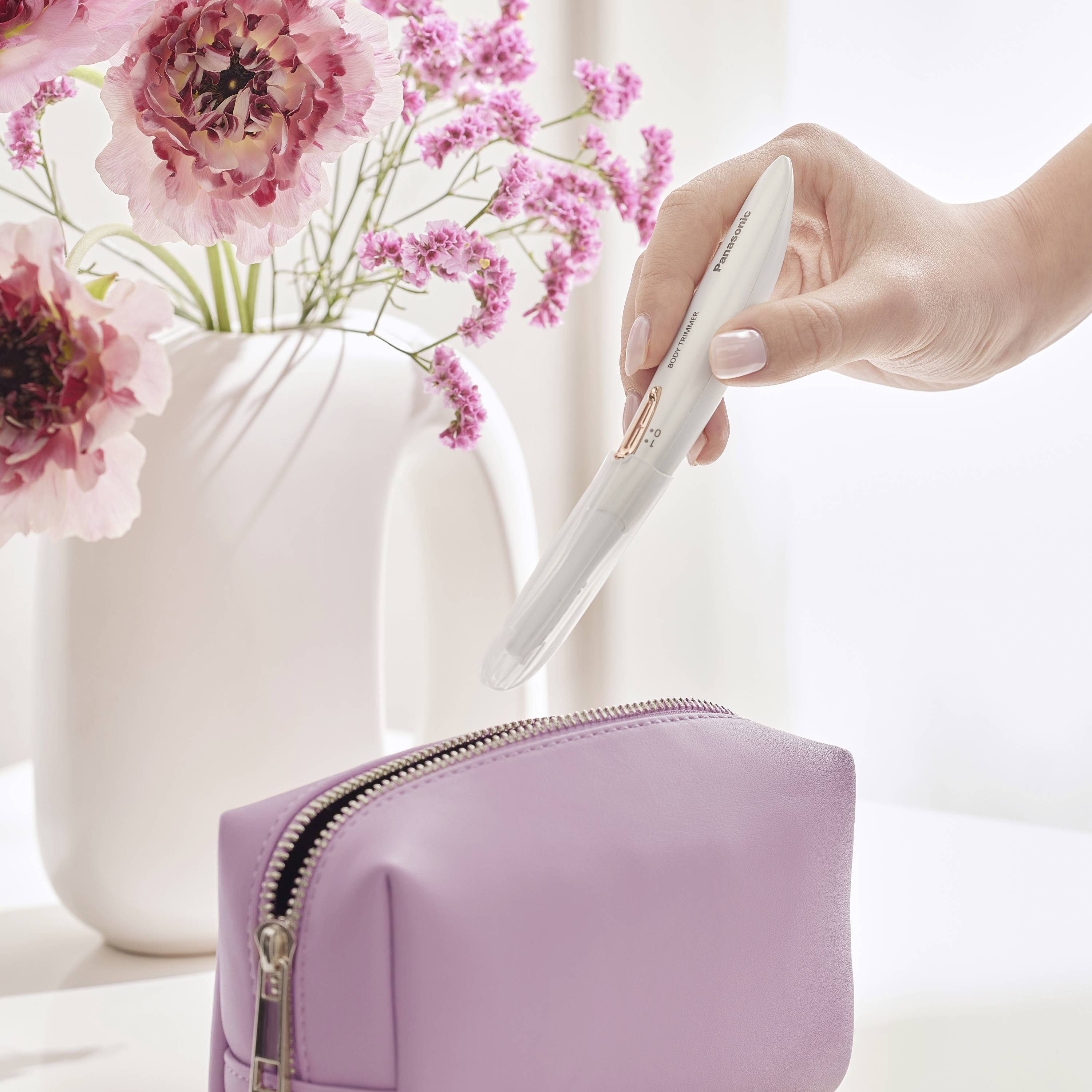 Une main tient un test de grossesse au-dessus d'un sac violet, avec des fleurs roses en arrière-plan dans un vase blanc.