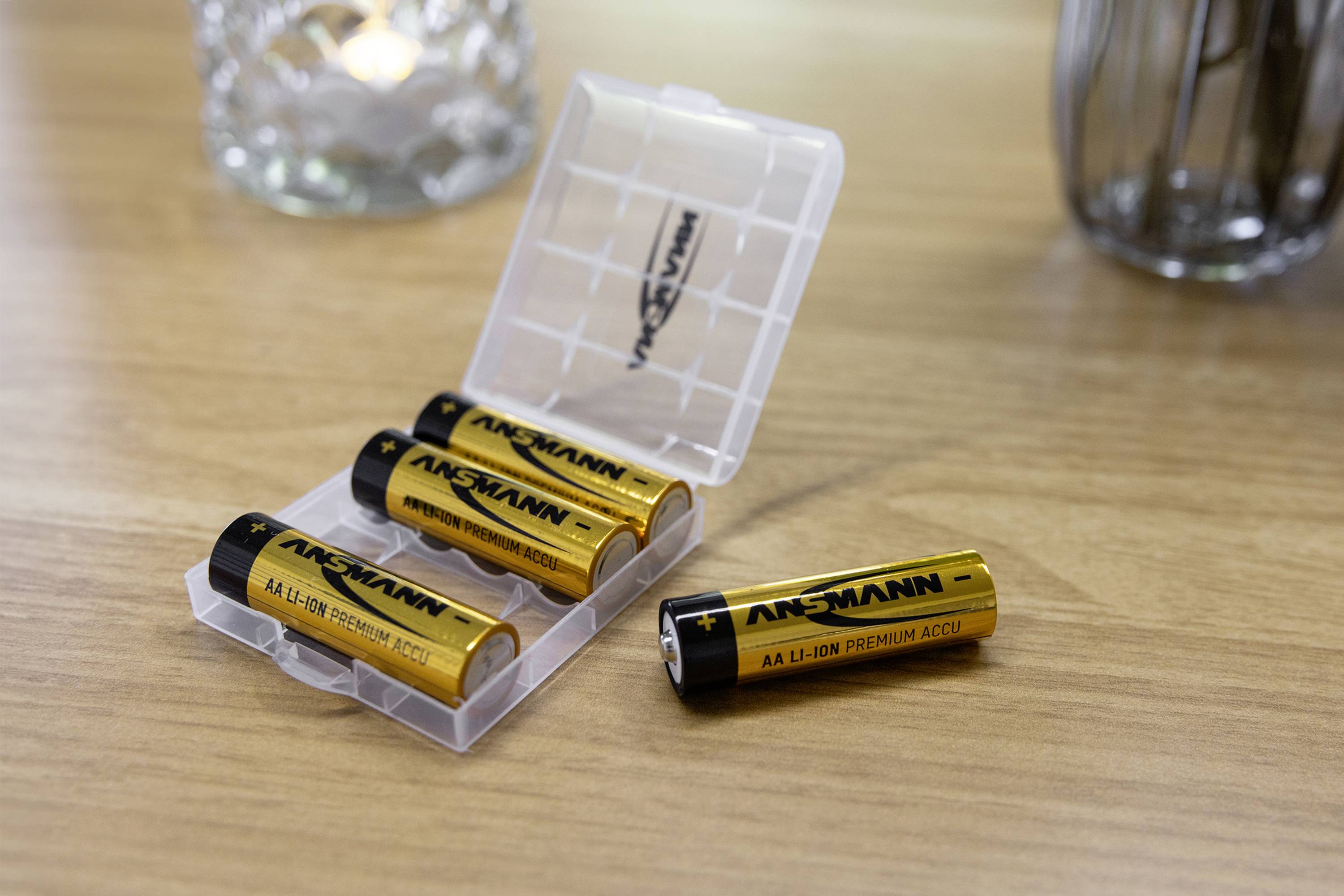 Quatre piles lithium-ion AA dans un boîtier en plastique ouvert sur une table en bois. Une batterie est placée à l'extérieur du boîtier.