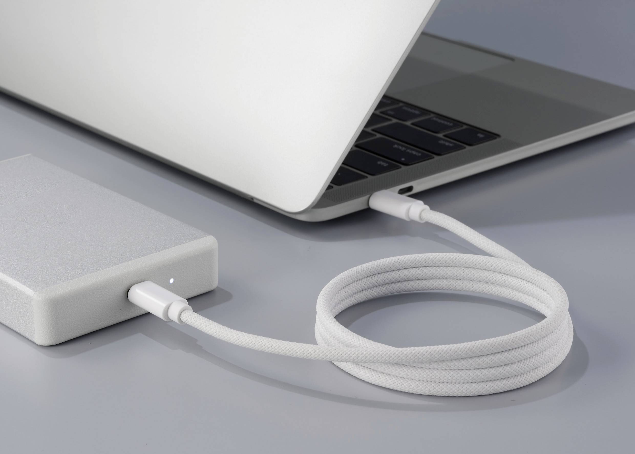 Un ordinateur portable est connecté à un disque dur externe via un câble de charge blanc.