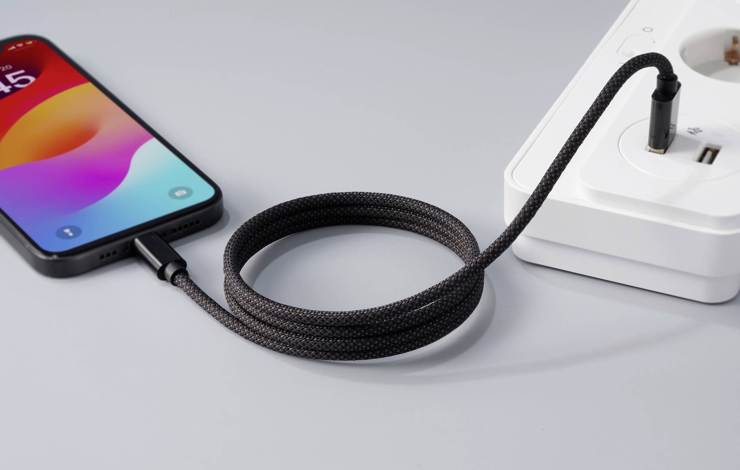 Un smartphone est en train de se charger avec un câble de charge tressé sur une multiprise blanche.