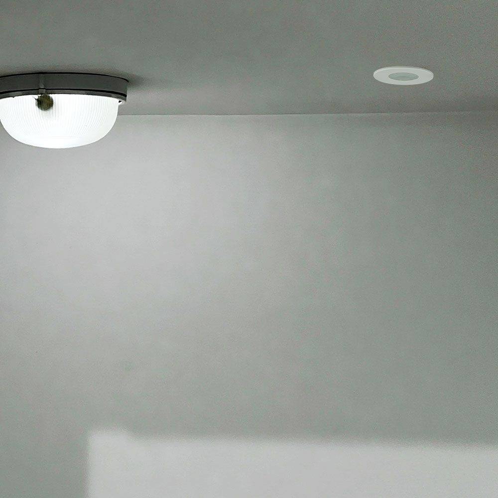 Plafond équipé d'un luminaire circulaire et d'un détecteur de fumée, au design épuré dans une pièce aux murs gris.