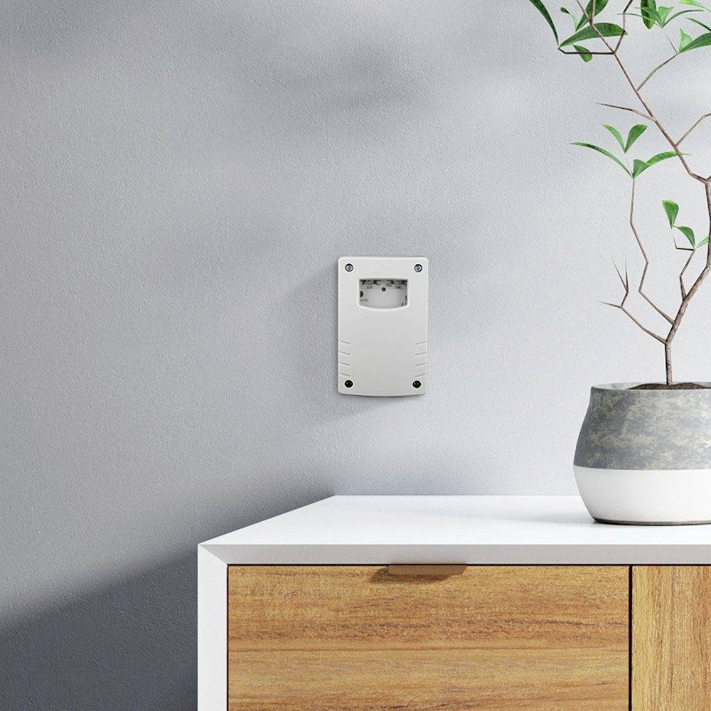 Un armoire en bois fermée devant un mur gris, avec un détecteur de fumée et une plante en pot posés dessus.