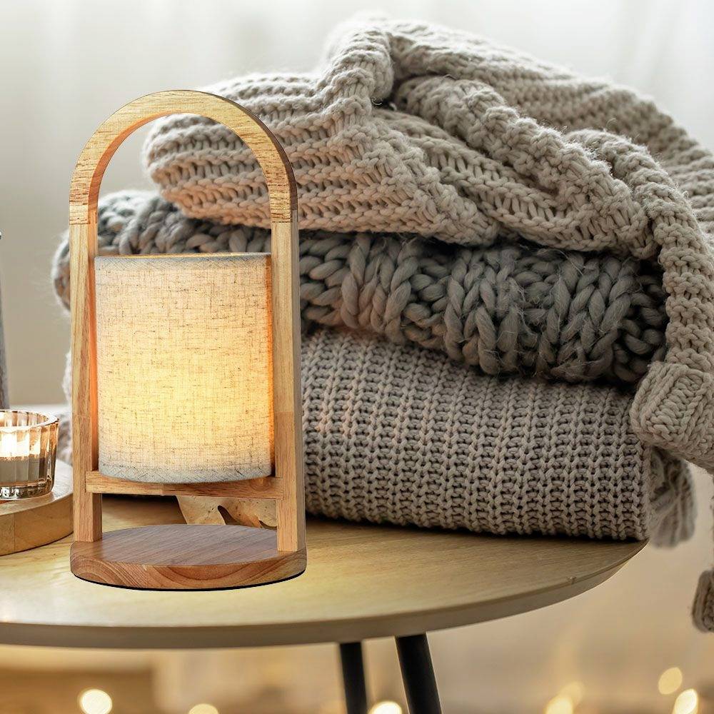 Une table ronde avec une lampe décorative en bois et en tissu, à côté de couvertures tricotées pliées dans des tons apaisants, qui créent une ambiance chaleureuse.
