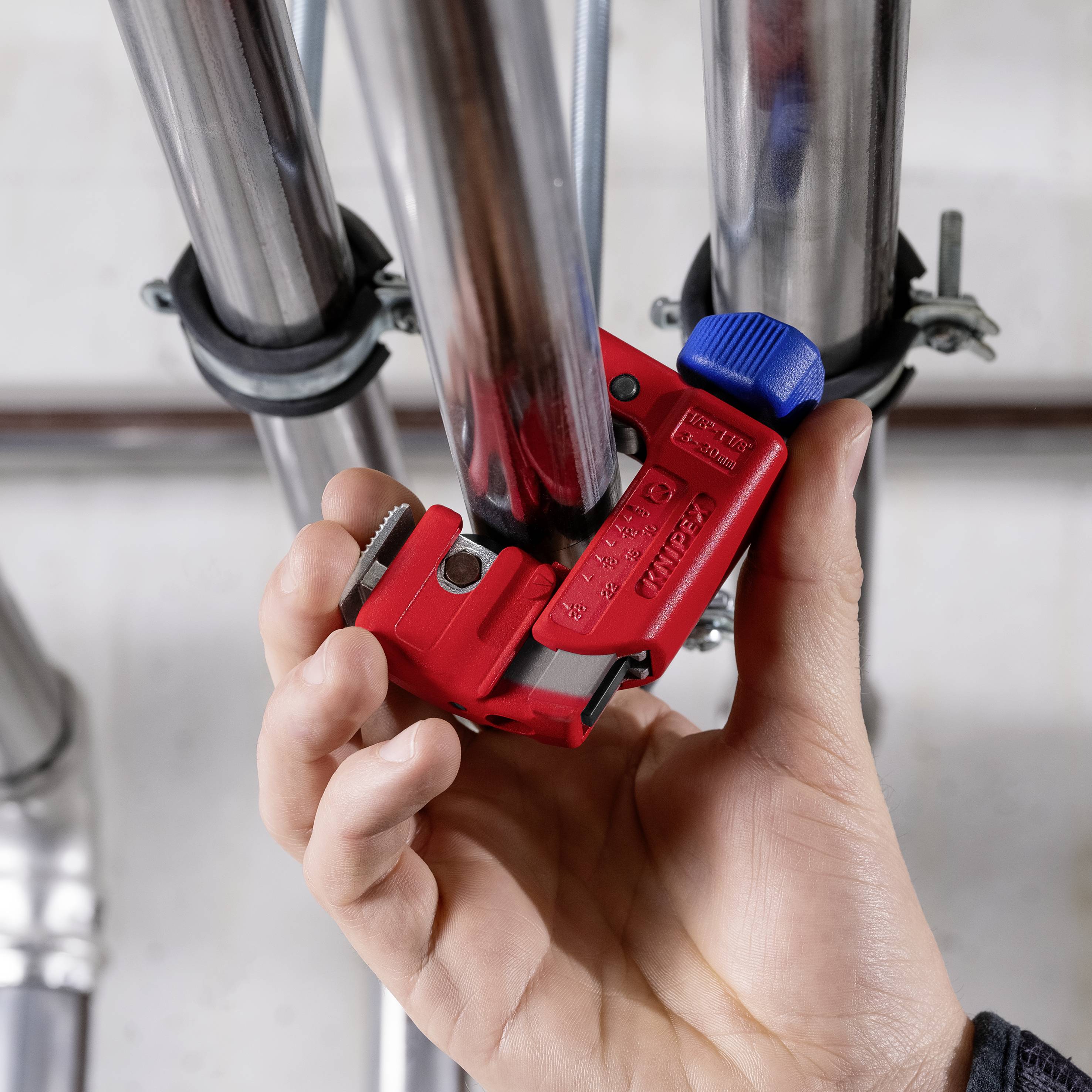 Une main utilise un outil rouge avec une vis bleue pour assembler fermement deux tubes argentés.