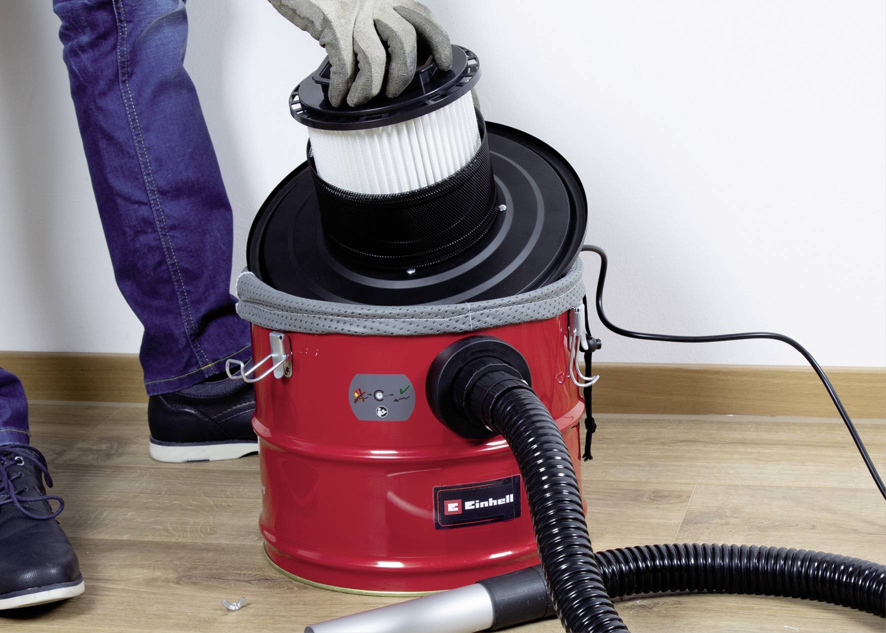 Une personne change le filtre d'un aspirateur rouge sur un sol en bois.
