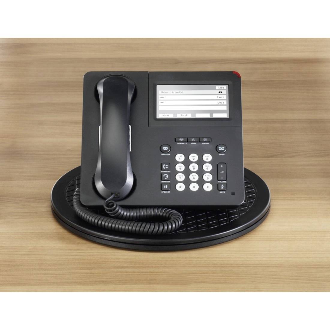 Un téléphone de bureau noir avec un écran et un clavier numérique est posé sur un dessous-de-plat rond sur une table en bois.