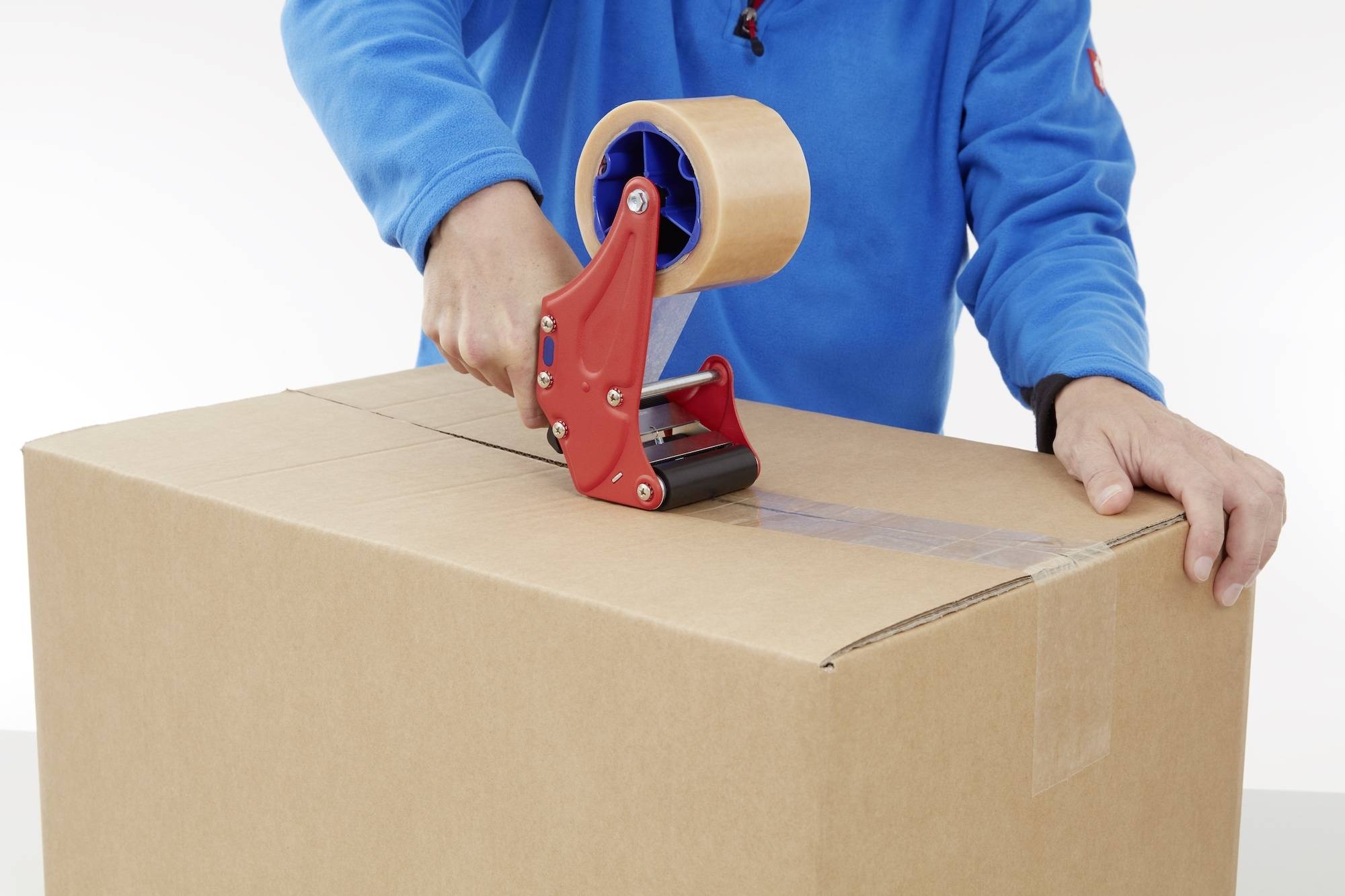 Une personne portant un t-shirt bleu scelle un grand carton avec du ruban adhésif.