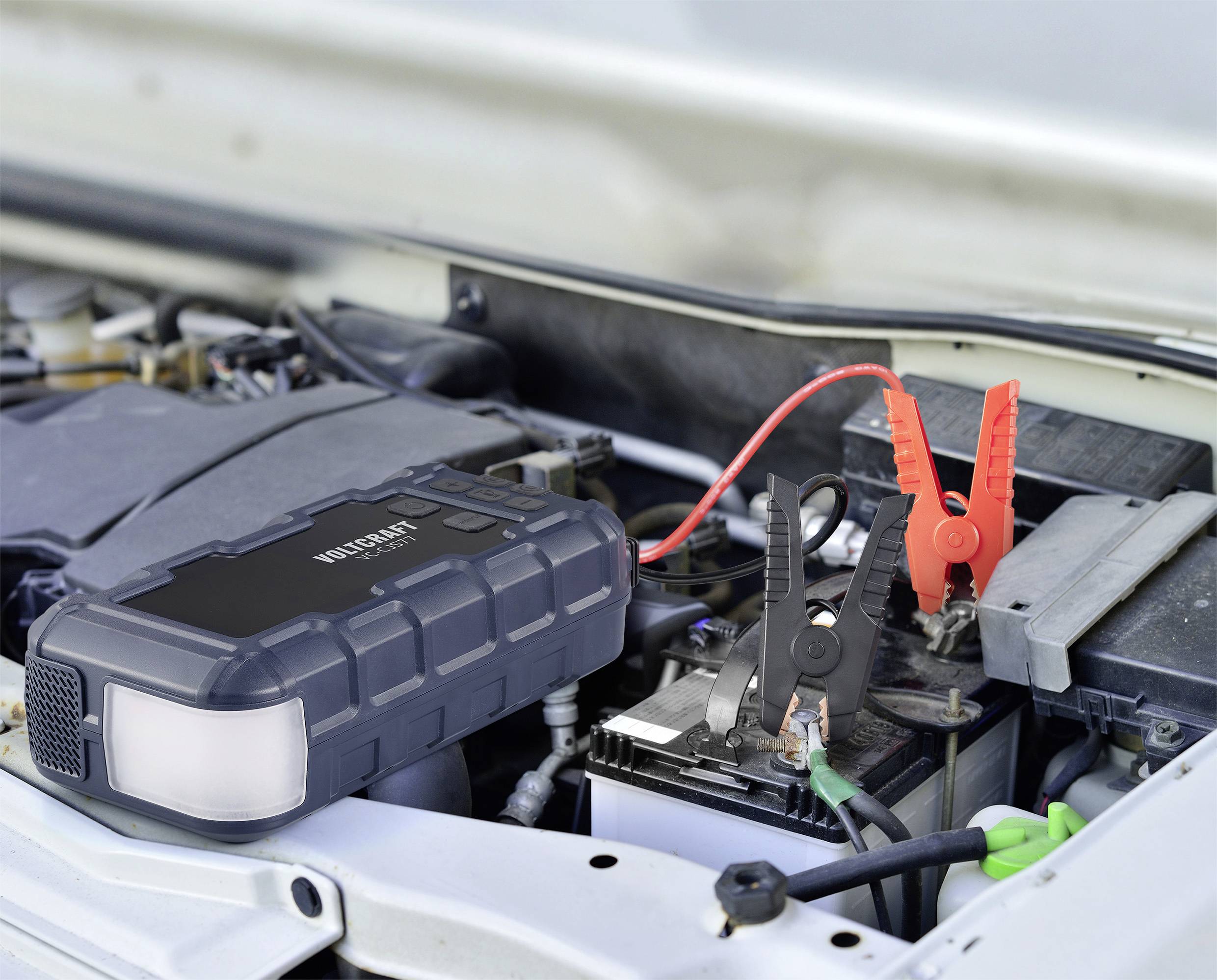 Un dispositif de démarrage est connecté à une batterie de voiture pour fournir du courant. Le câble rouge et le câble noir sont fixés aux bornes de la batterie.