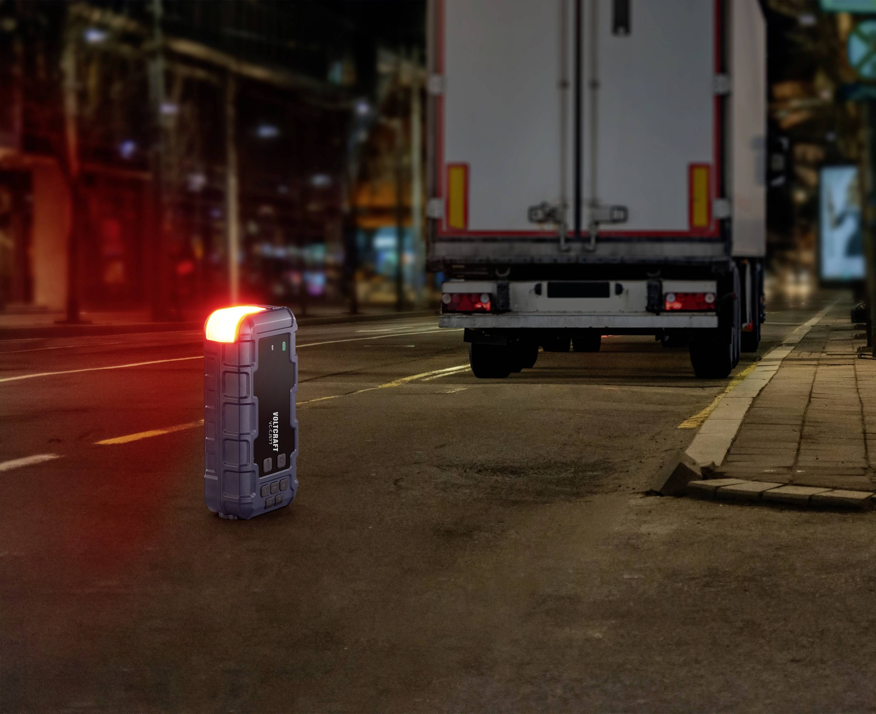 Une petite valise lumineuse est posée sur la route, la nuit, devant un camion stationné. La scène est urbaine et éclairée.