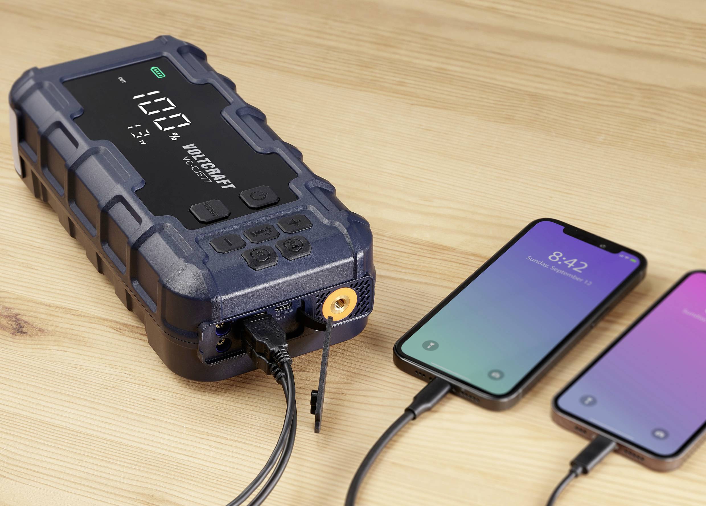 Un chargeur portable charge deux smartphones. L'écran affiche '100%', indiquant que l'appareil est complètement chargé.
