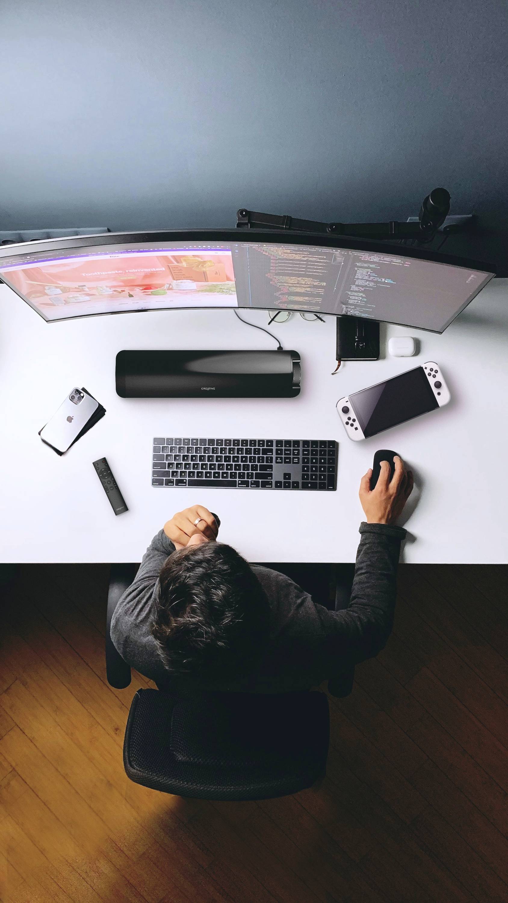 Personne assise à un bureau avec un poste de travail à double écran, travaillant sur ordinateur. Sur le bureau sont visibles un smartphone, un clavier et une souris.