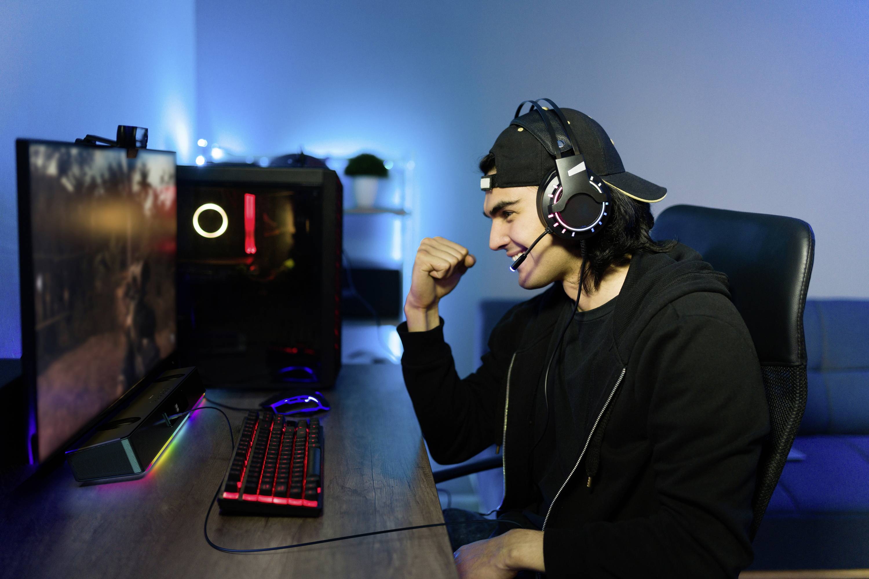Un jeune homme est assis devant un écran d'ordinateur, portant un casque audio et souriant pendant qu'il joue à un jeu vidéo.