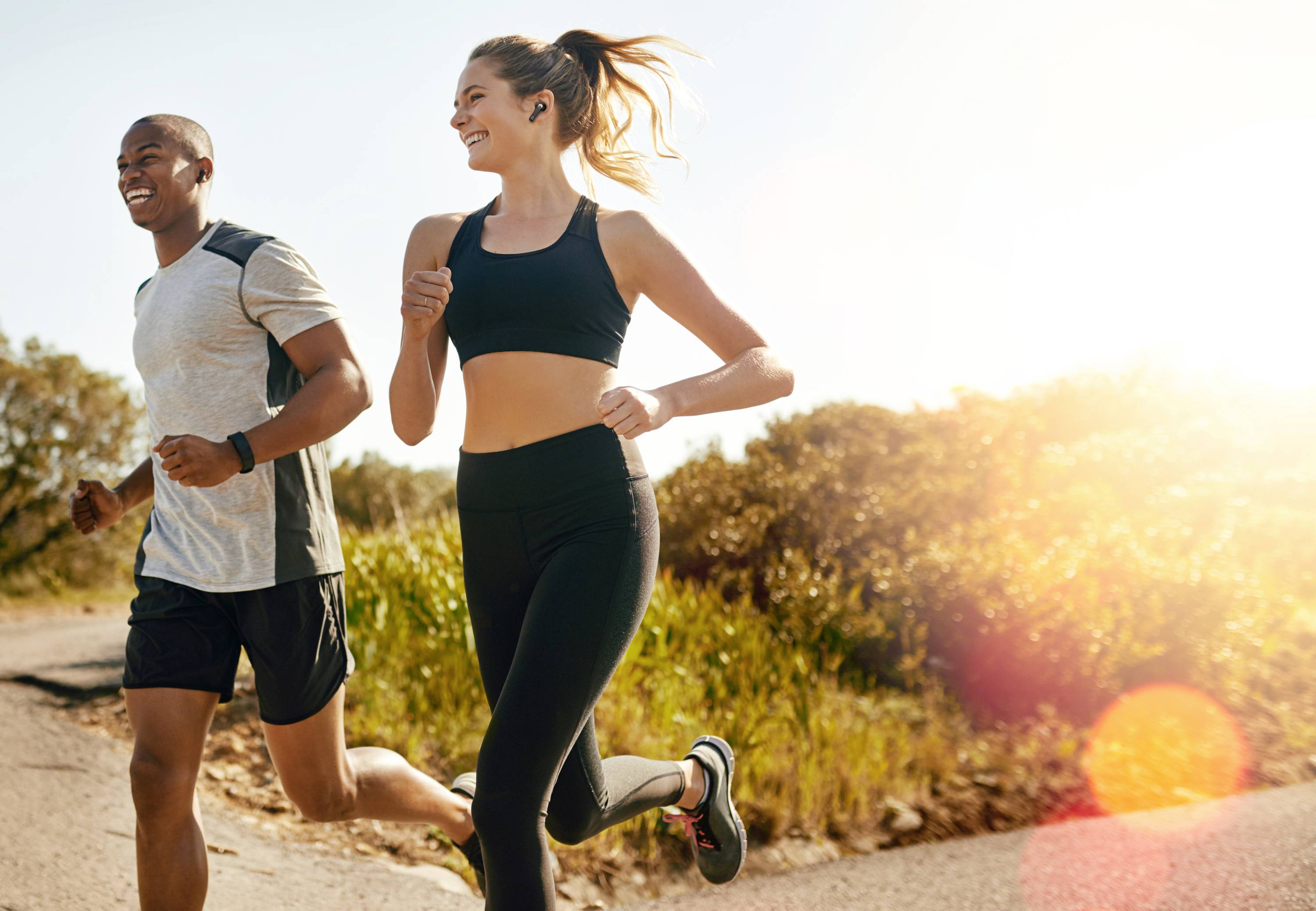 Deux personnes font joyeusement du jogging par une journée ensoleillée sur un chemin de campagne, entourées de végétation verdoyante.